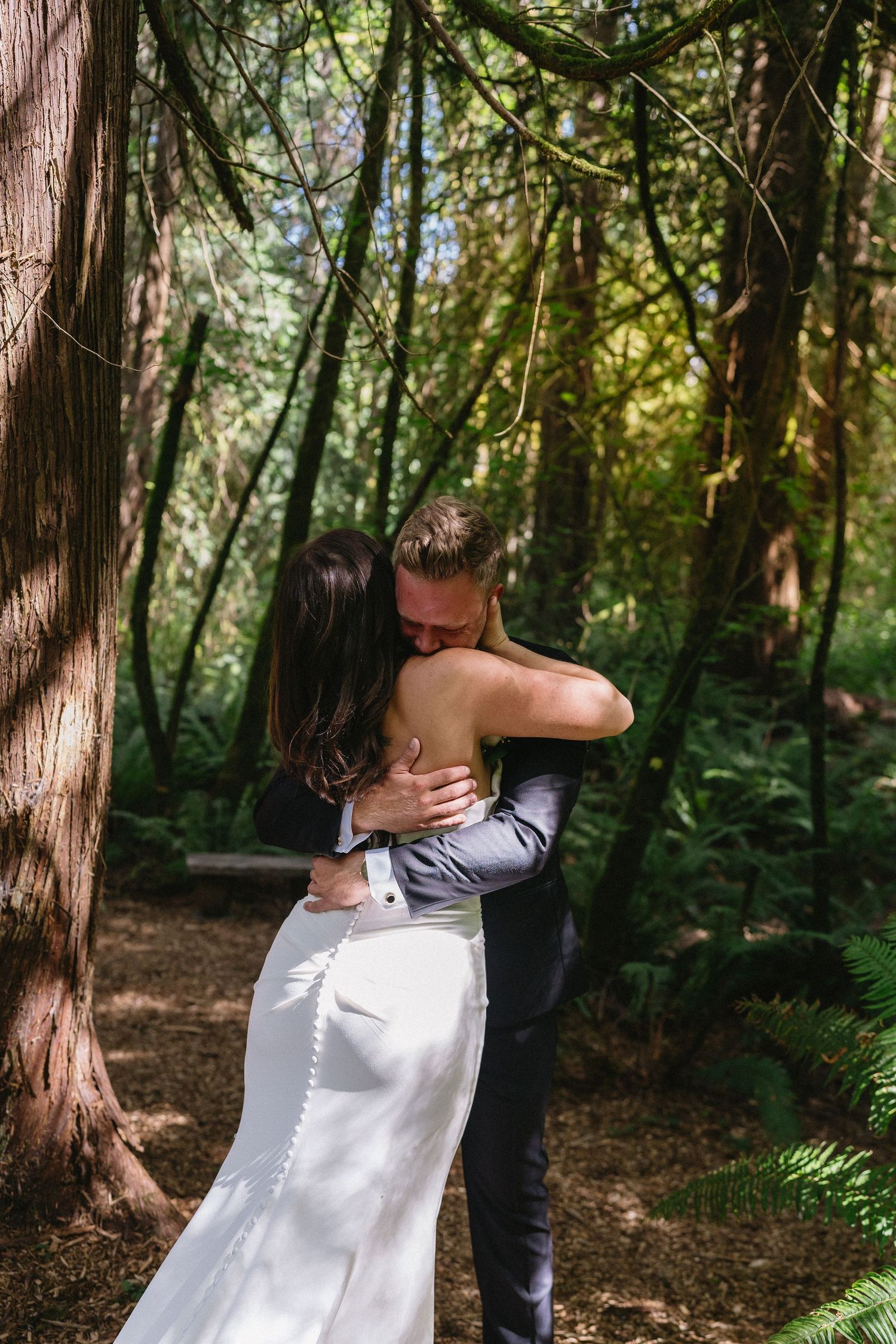 Bride and groom share first look embrace in lush green forest.