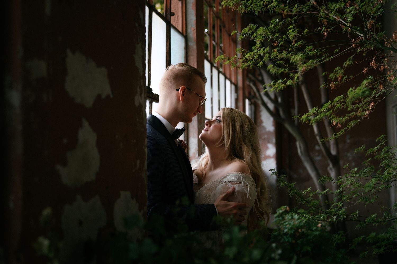 Romantic couple sharing intimate moment near rustic window surrounded by lush greenery.