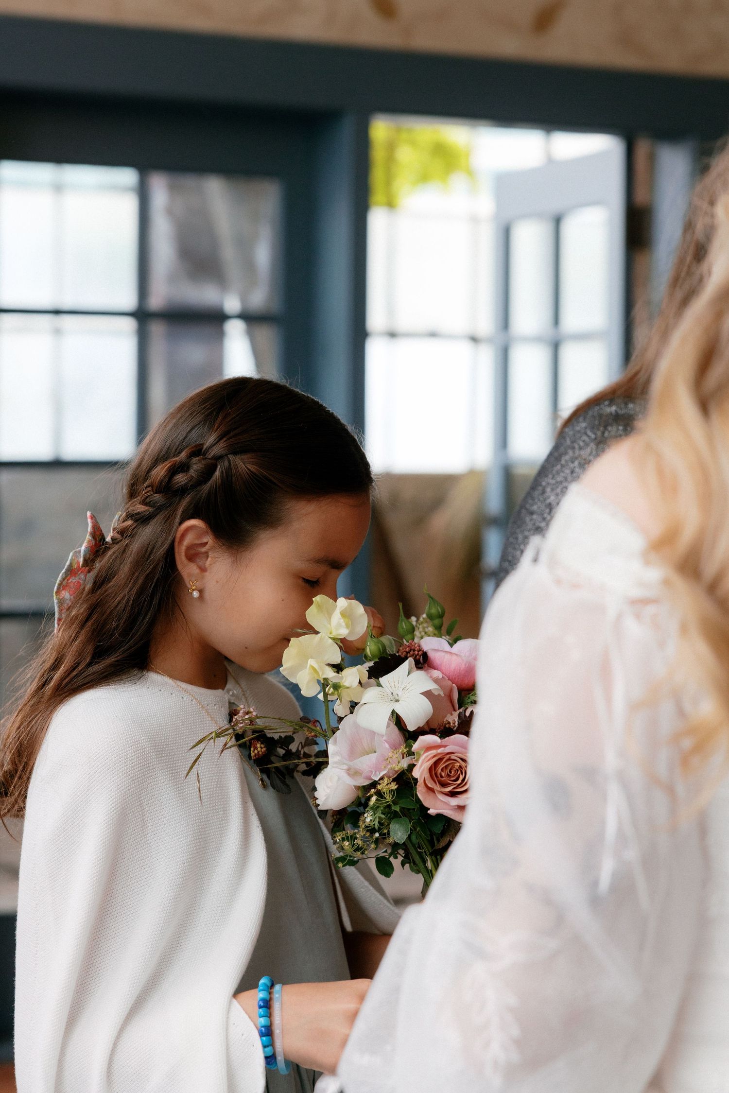 Young flower girl smelling bridal bouquet of pink and white roses at wedding ceremony.