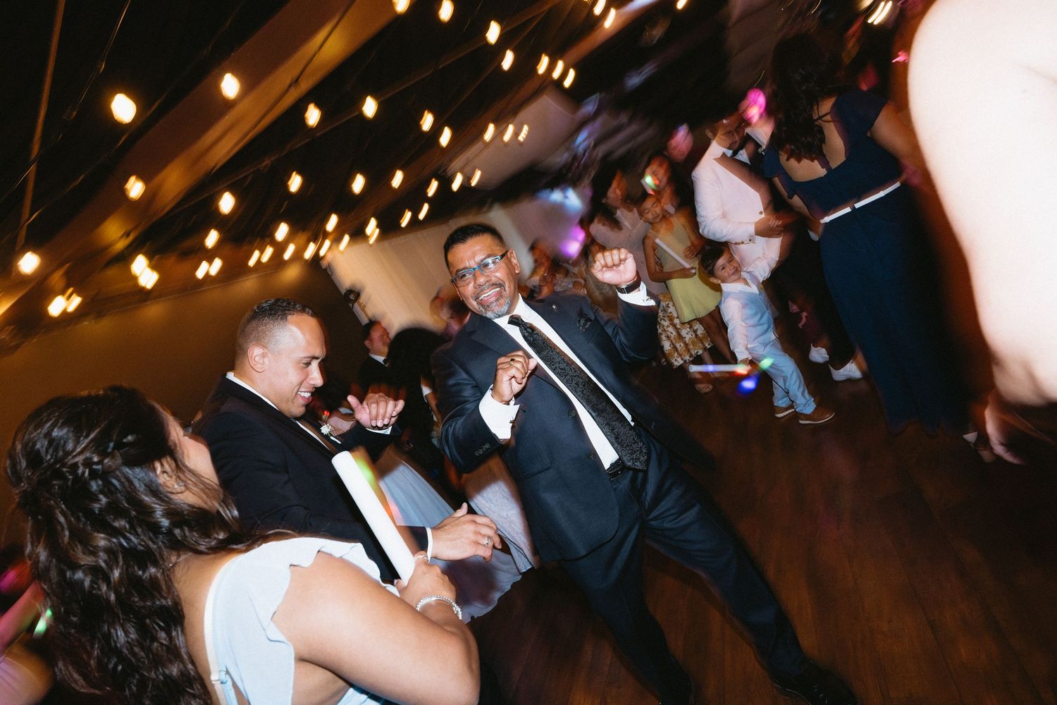 Wedding guests and groom celebrate on the dance floor with glow sticks at a fun reception.