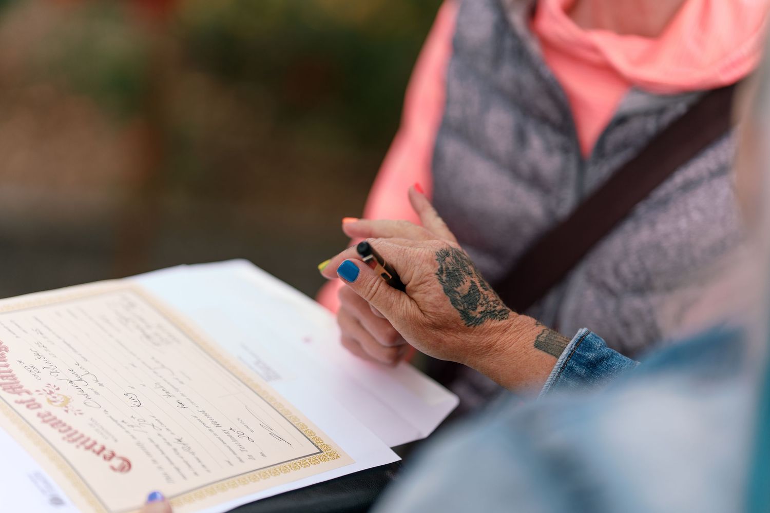 Close-up of officiant holding marriage certificate with tattooed hands during wedding ceremony.