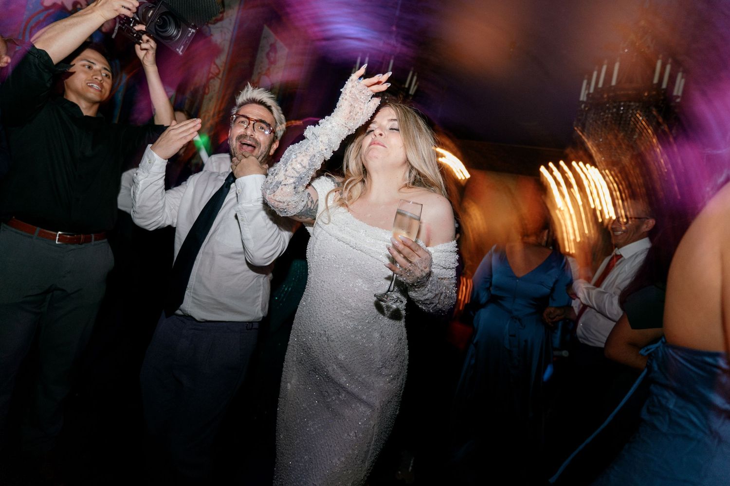 Bride in white dress dancing energetically with guests at a festive wedding reception.