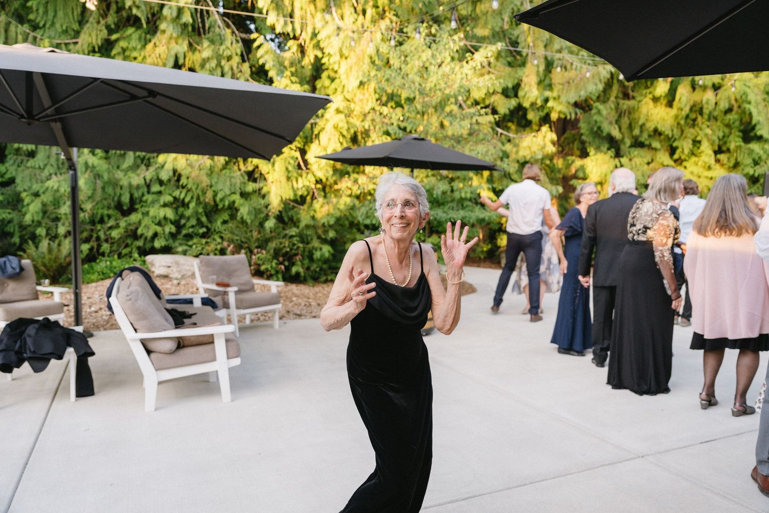 Joyful older woman in black dress dancing and waving at outdoor wedding reception party.