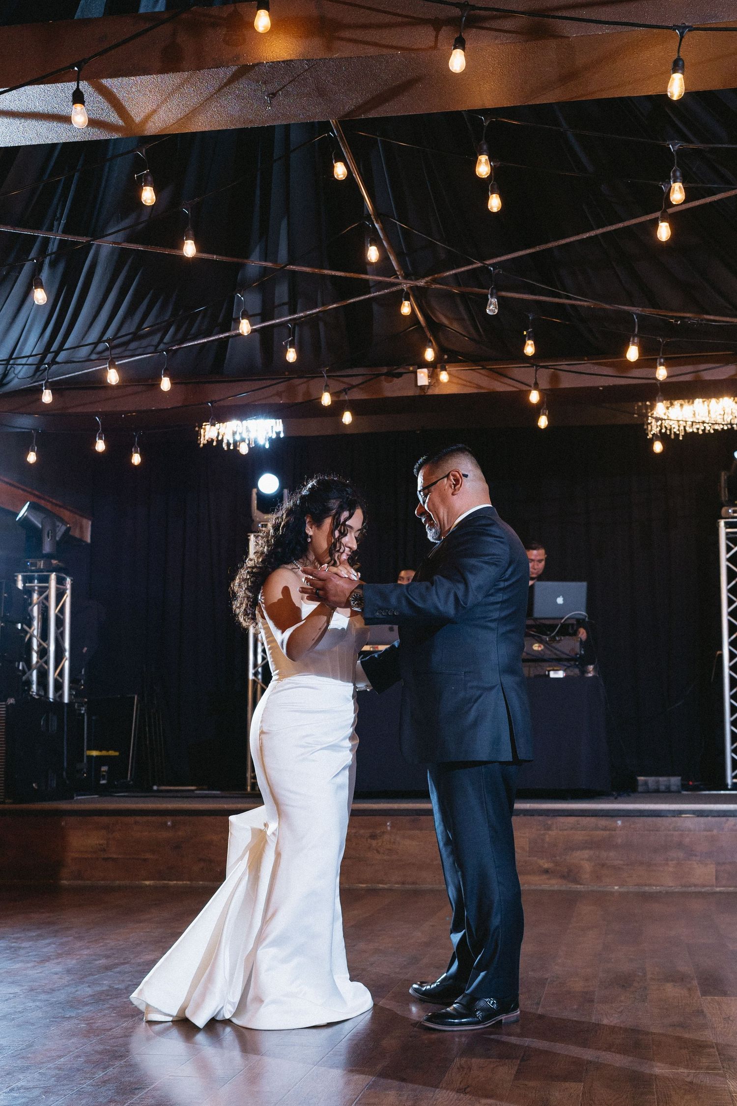 Bride and father sharing emotional father-daughter dance under warm string lights at reception.