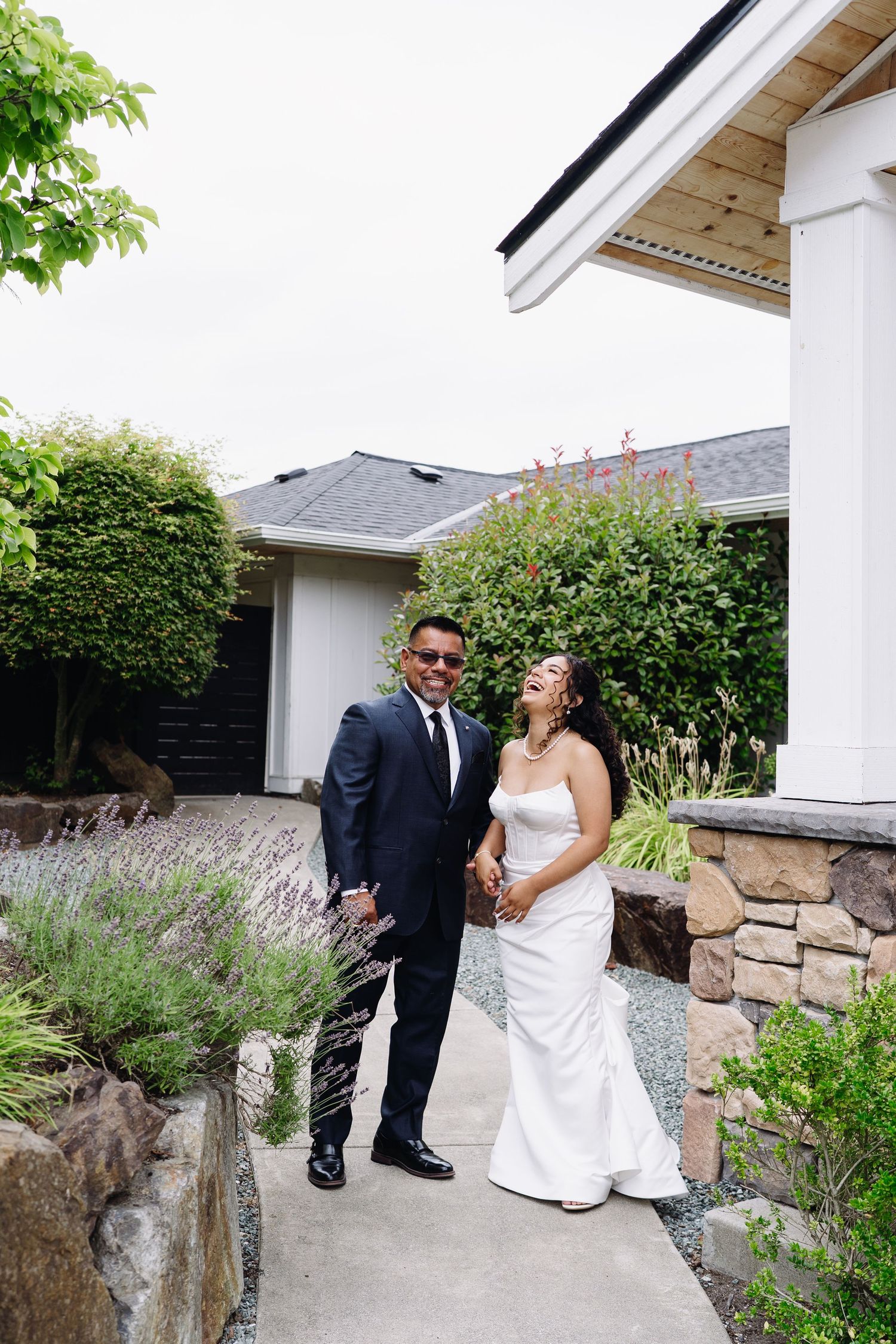 Smiling bride and groom holding hands outside venue surrounded by lush garden greenery.