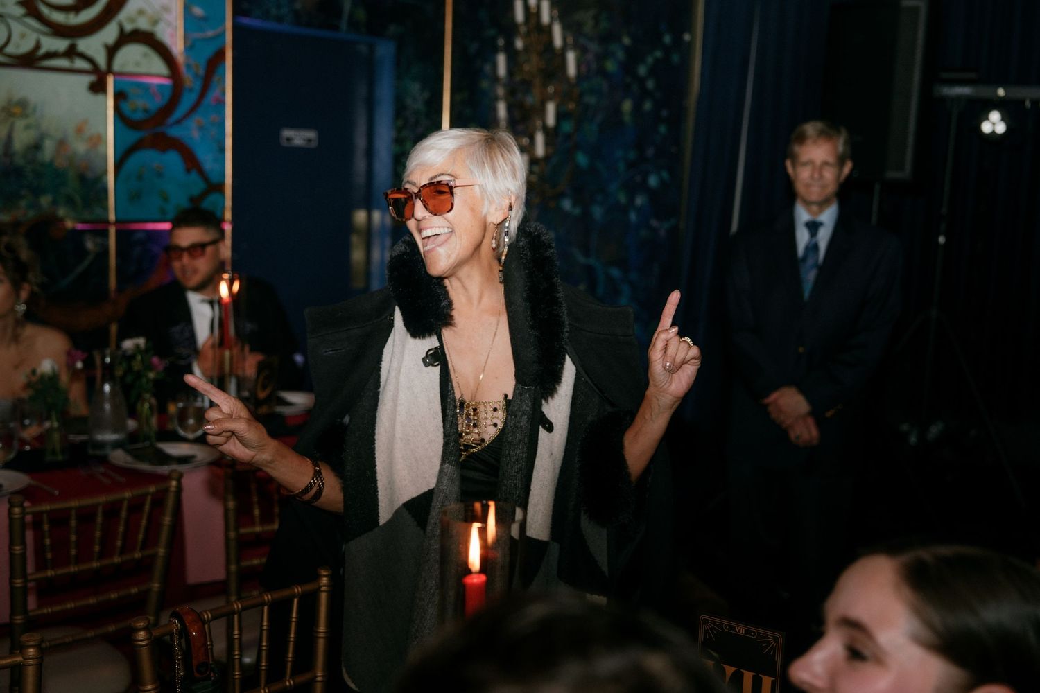 Stylish woman with white hair and oversized sunglasses dancing at wedding reception.