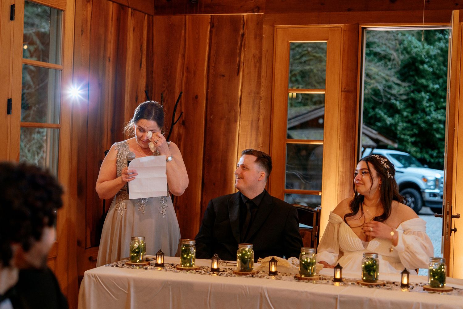 Bridesmaid gives emotional speech at wedding reception while bride and groom sit at head table.