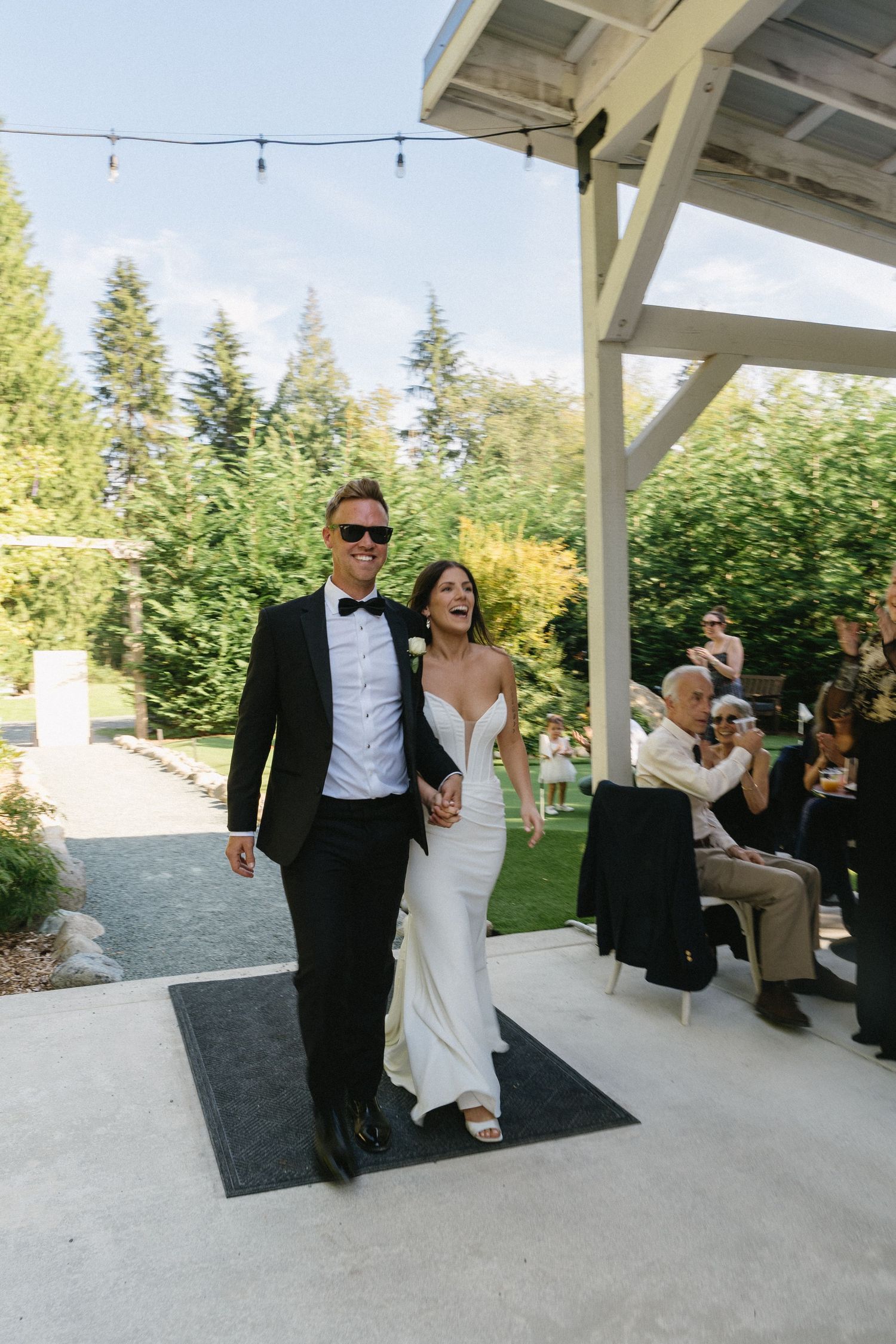 Newlywed couple walking hand in hand smiling at their outdoor wedding reception entrance.