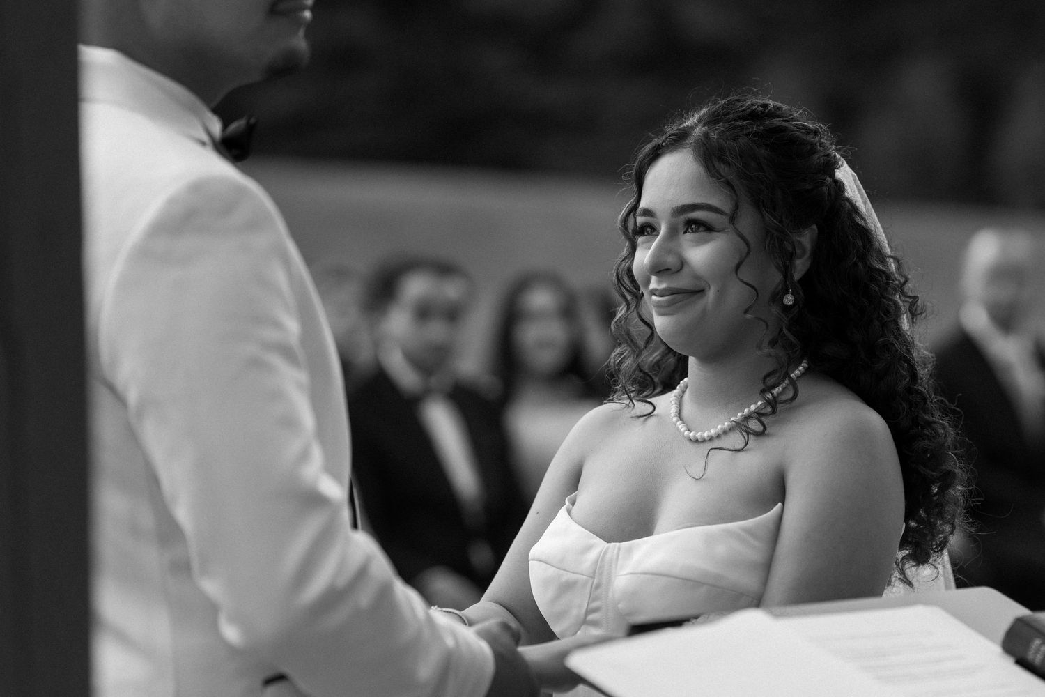 Black and white portrait of a smiling bride holding hands with the groom during their wedding ceremony.