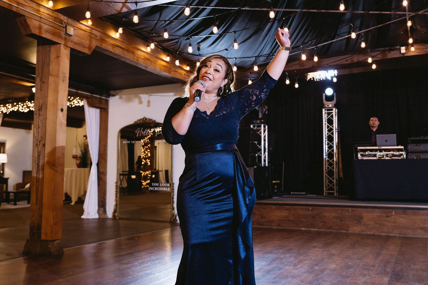 Woman in navy gown performing emotional song at wedding reception under string lights.