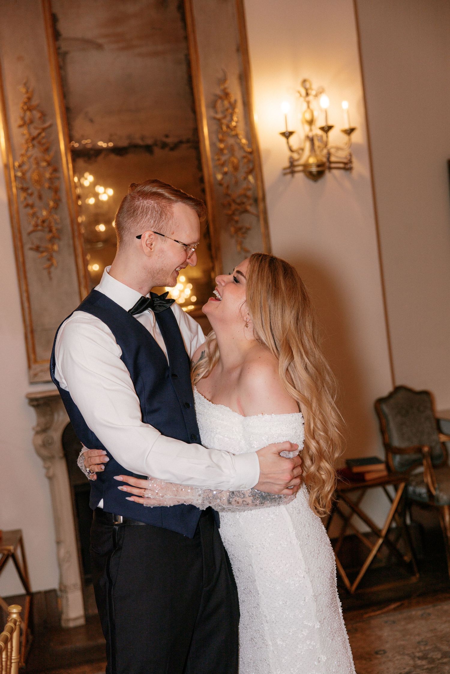 Bride and groom laughing together during first dance in an elegant golden ballroom with sconces.