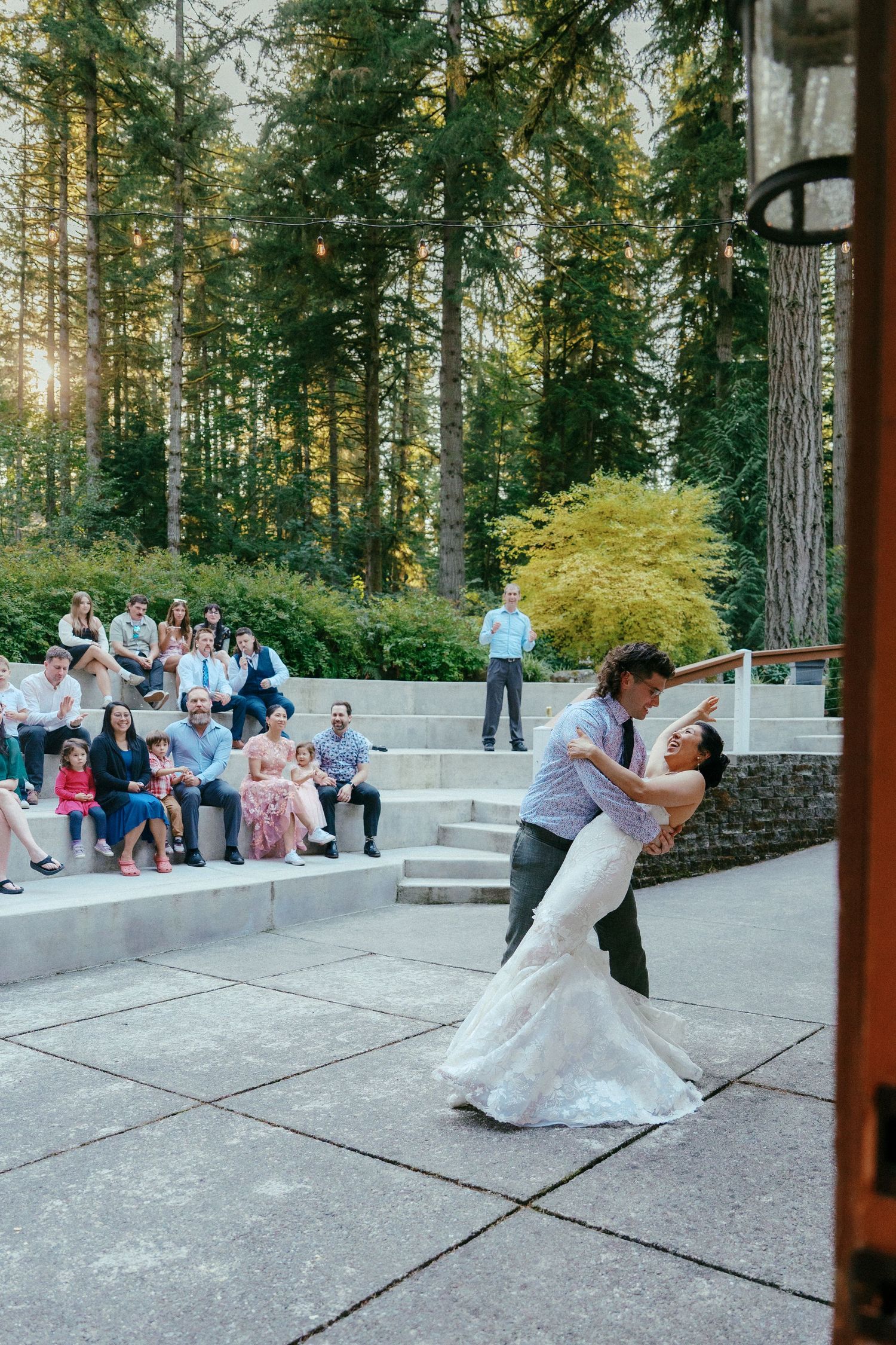 Groom dips bride in white mermaid gown during first dance at outdoor woodland wedding venue.
