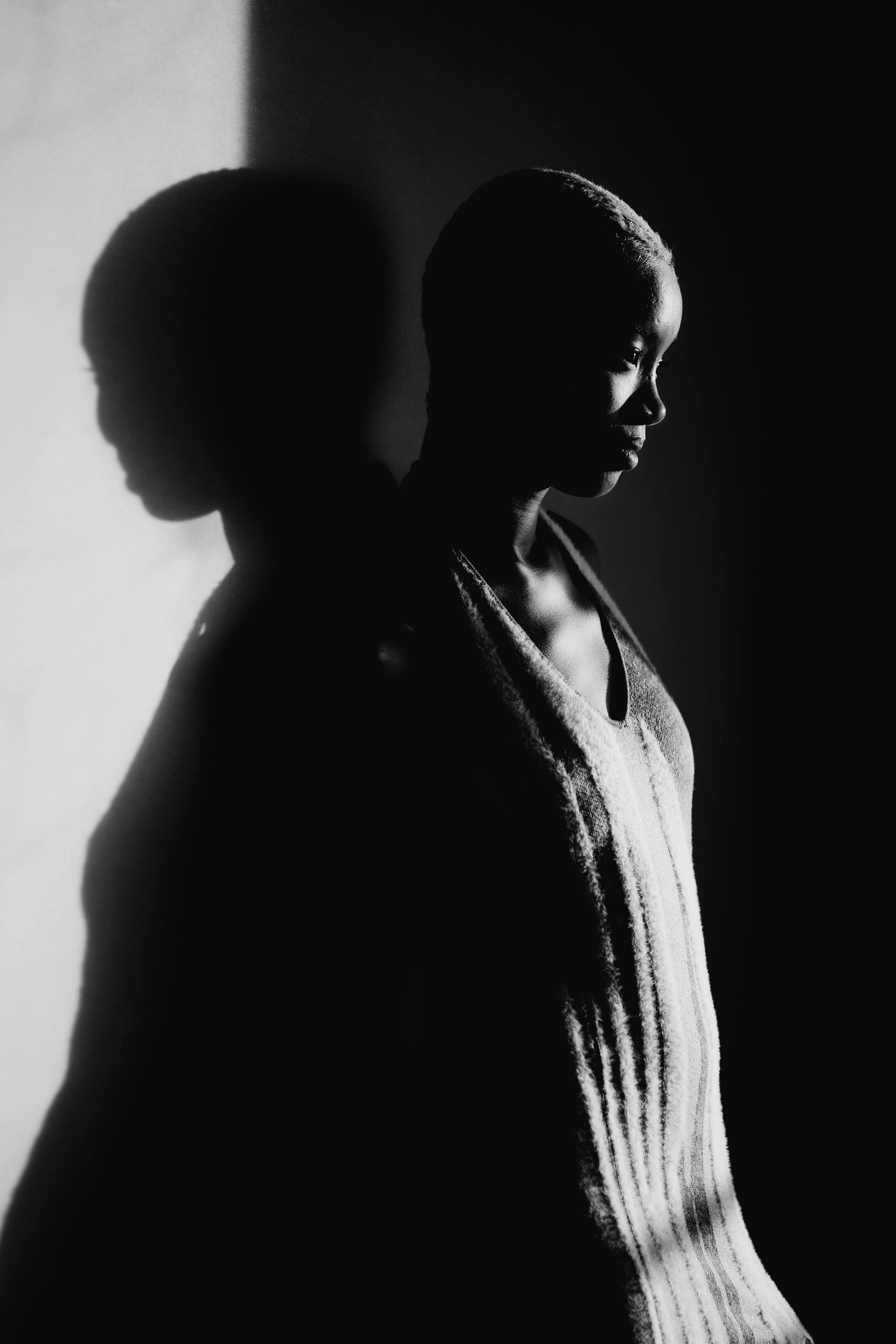 Dramatic black and white silhouette portrait of a woman in a striped dress with shadow against a light wall.