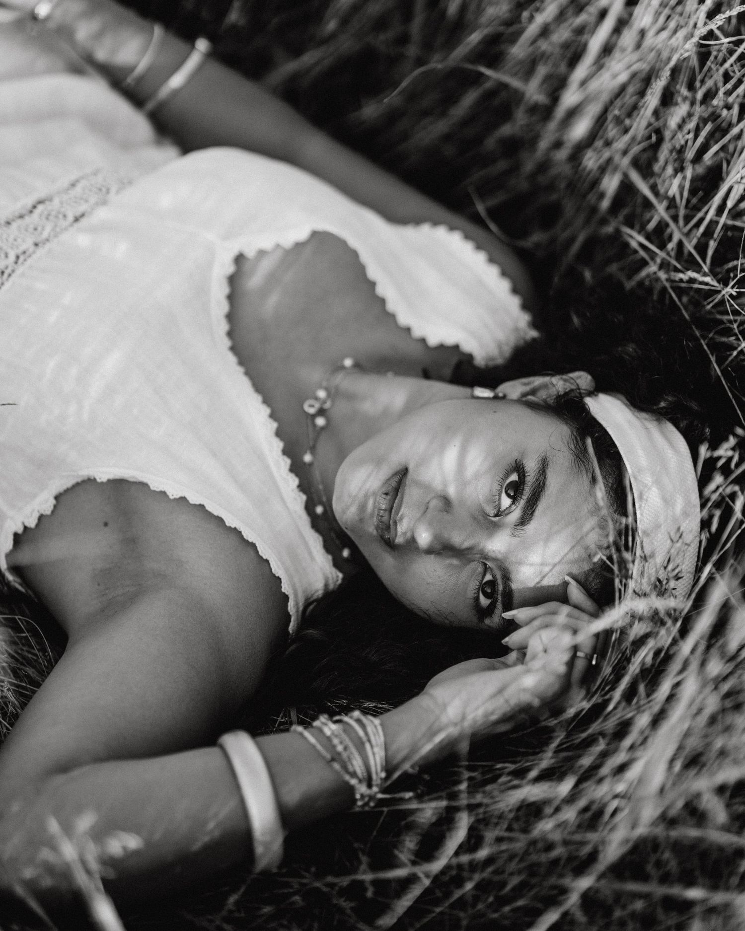 Black and white photo of woman in white dress lying in tall grass wearing headband.
