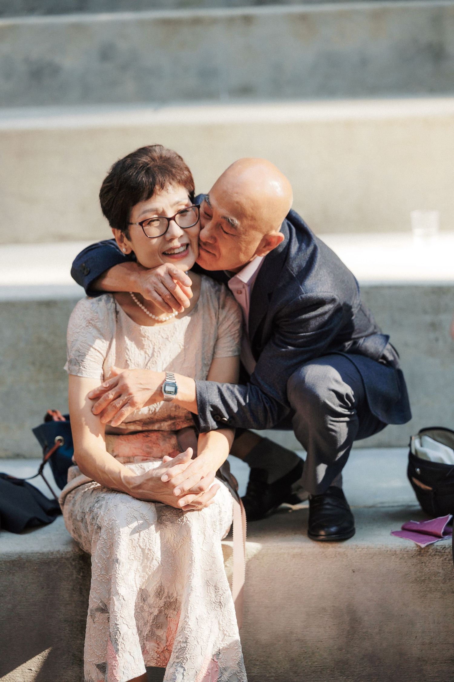 Elderly couple sharing a tender kiss moment, man in suit crouching to embrace seated woman.
