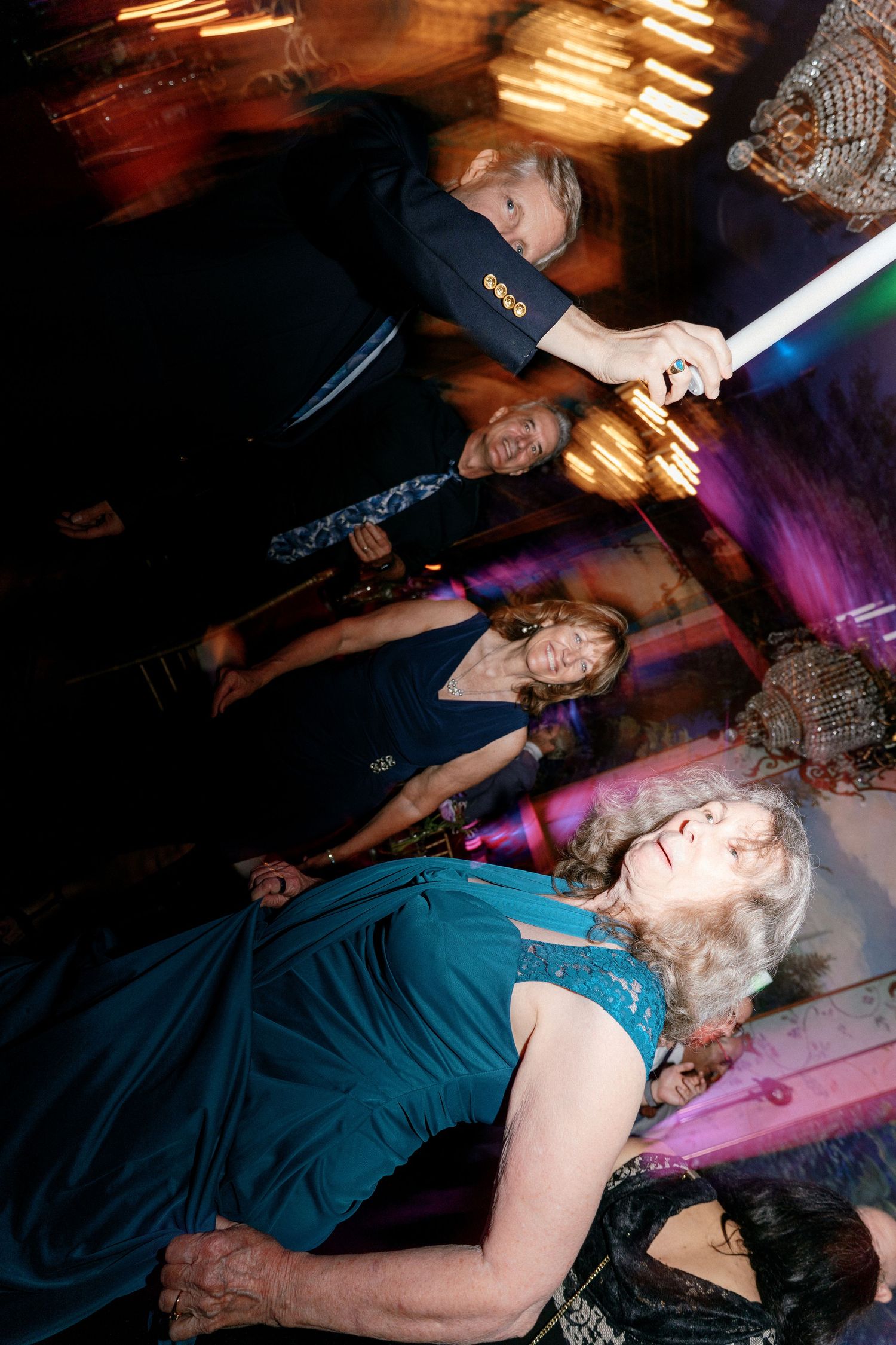 Wedding guests dancing with glow sticks at reception with motion blur effect.