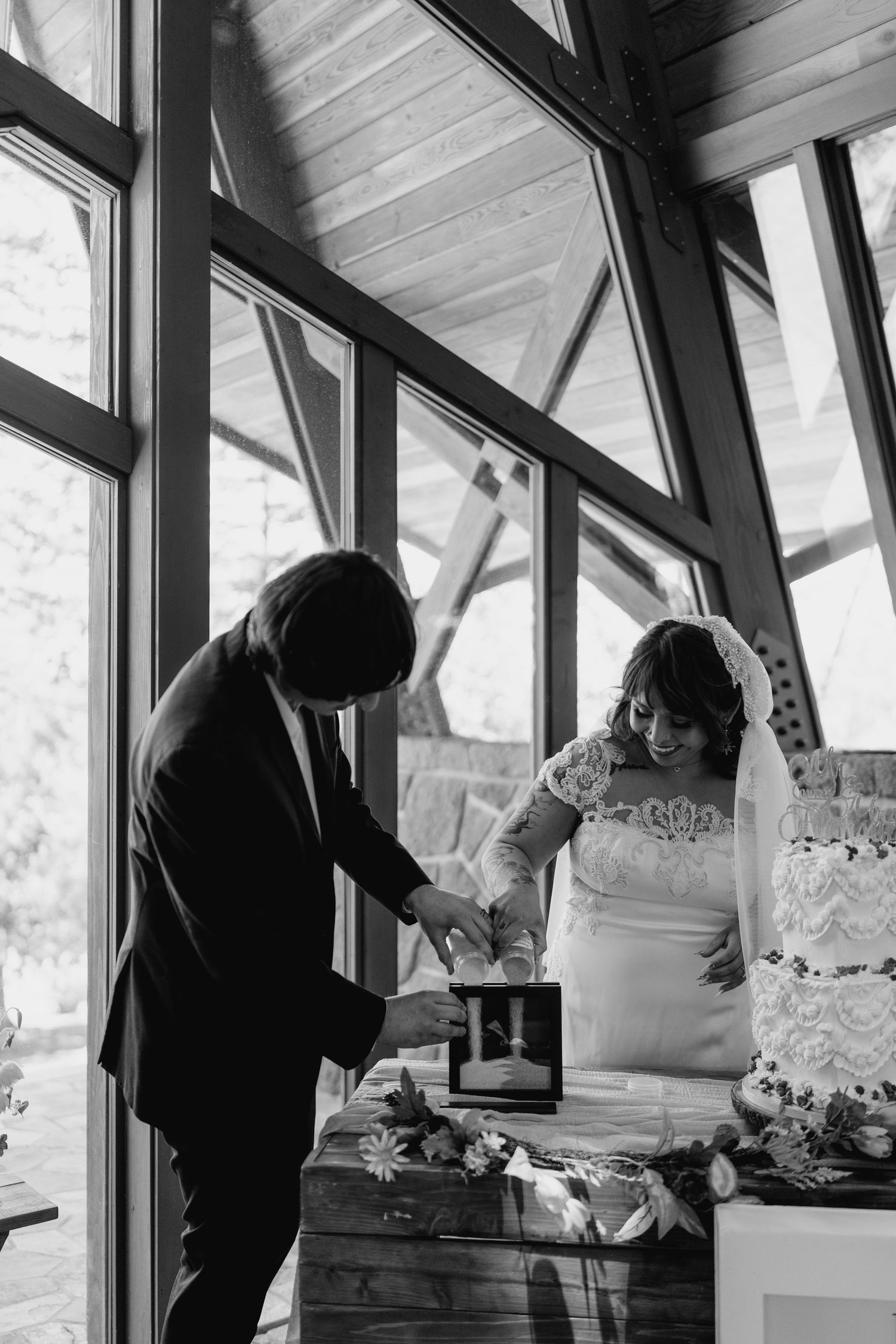 Black and white photo of bride and groom performing a sand ceremony at their wedding altar.