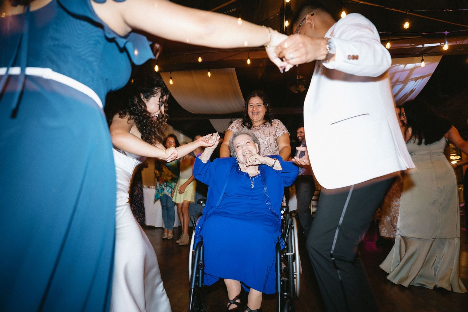 Elderly guest in wheelchair joyfully joins family members dancing at a lively wedding reception.