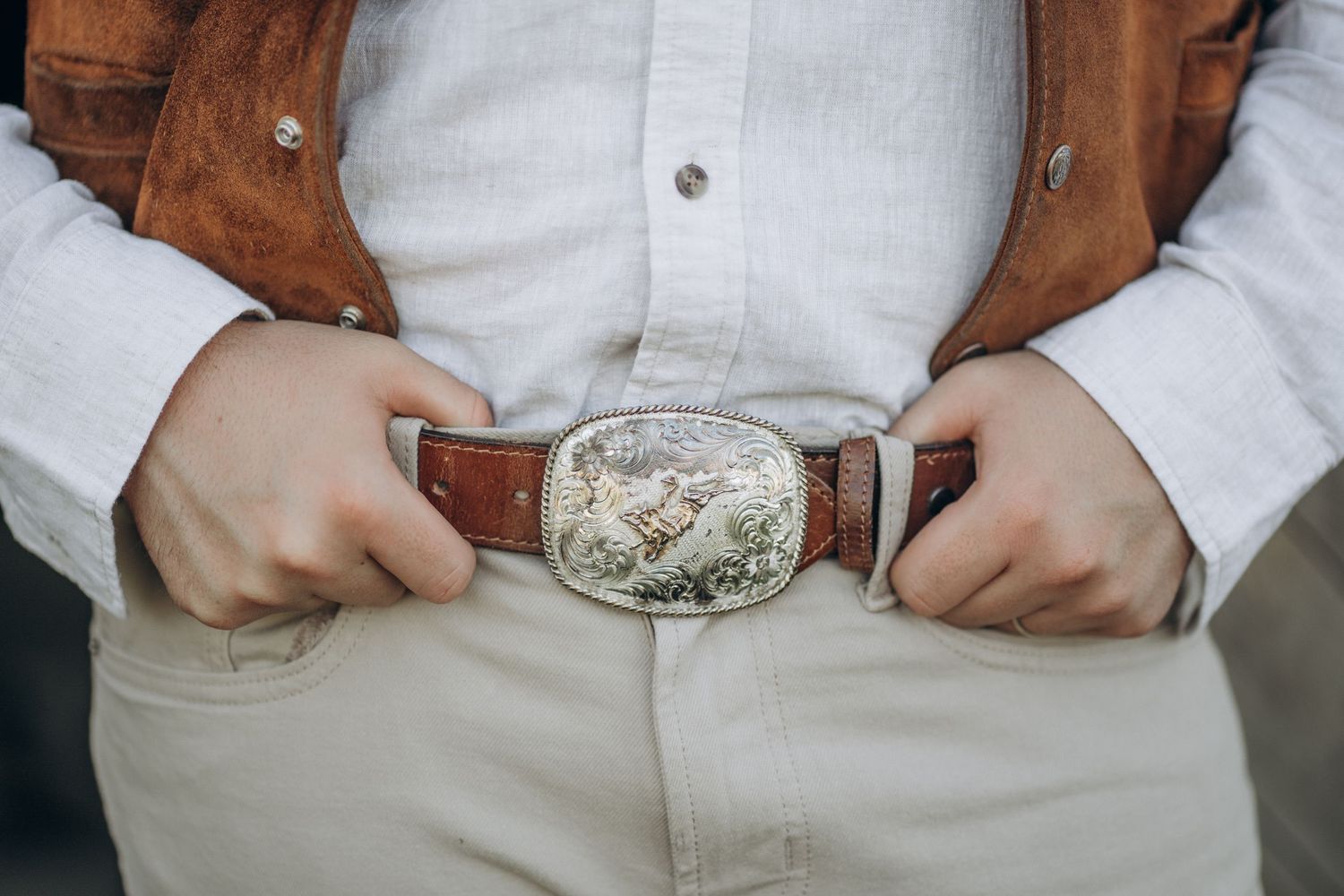 Close-up of groom wearing ornate silver western belt buckle with brown leather belt.