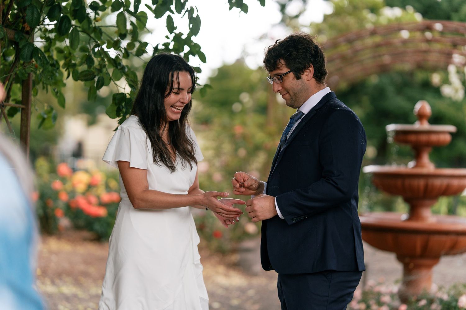 Bride and groom laughing joyfully during outdoor garden wedding ring exchange ceremony.