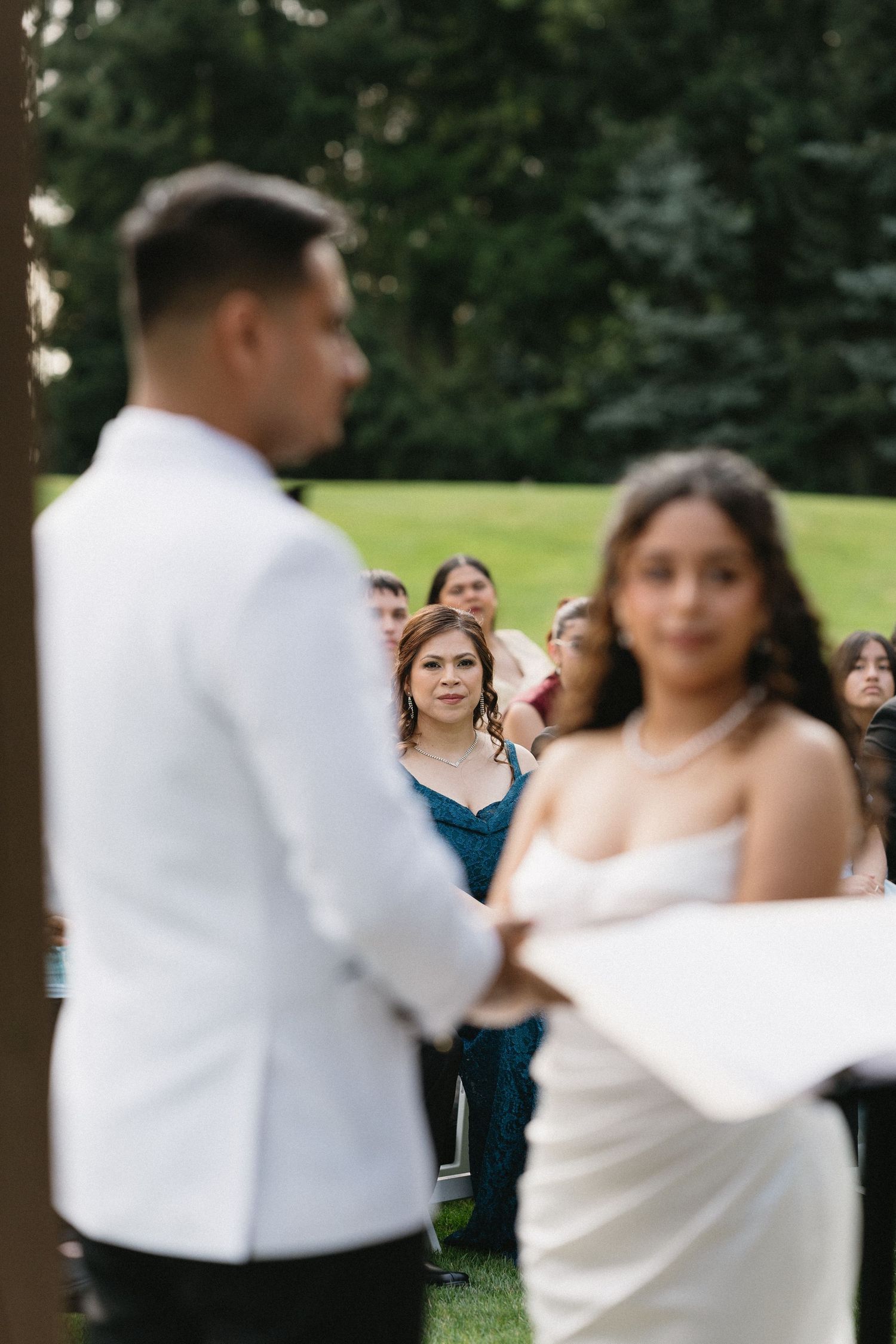 Wedding guests watch attentively as the bride reads her vows during an outdoor garden wedding ceremony.