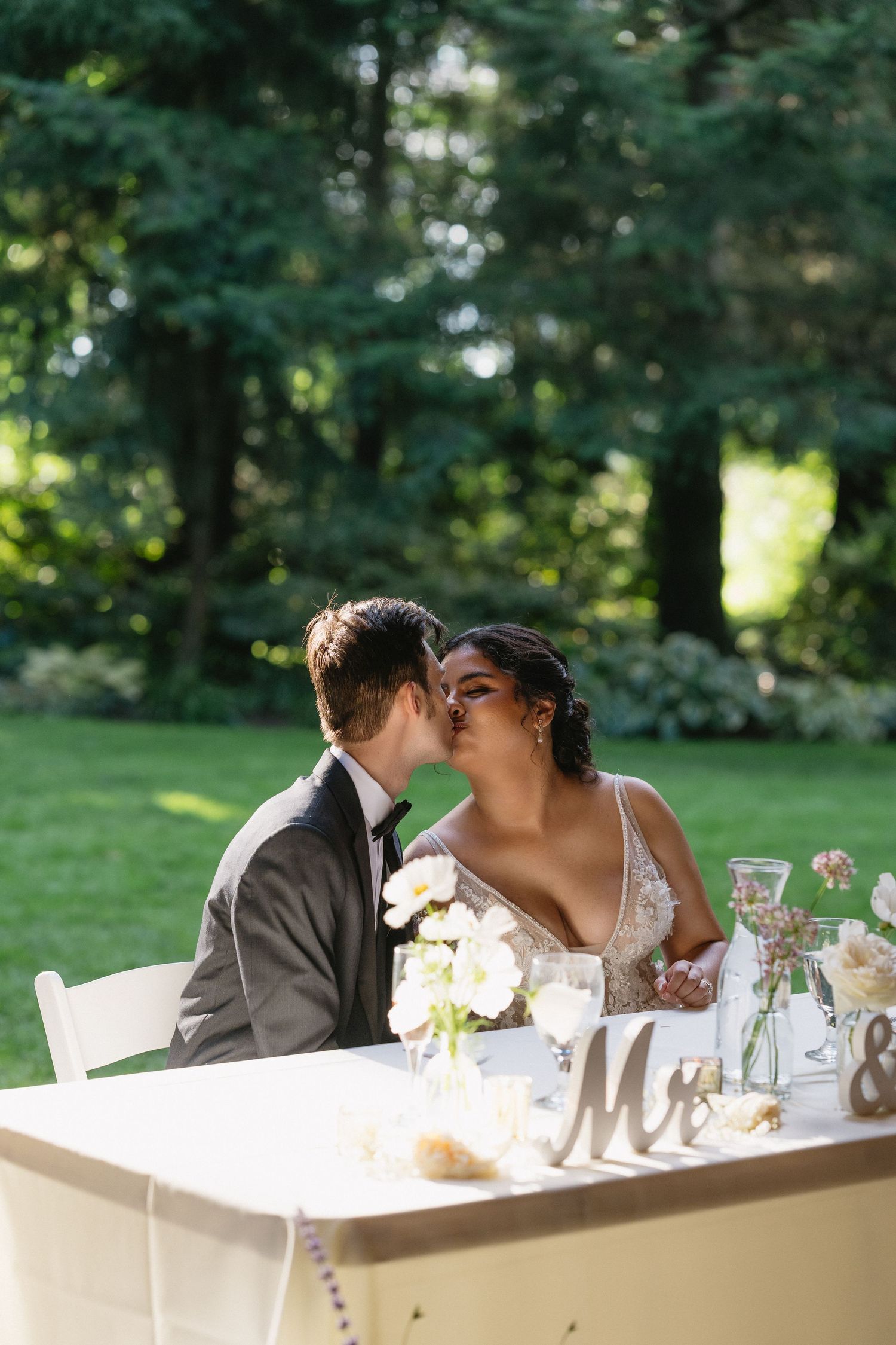 Bride and groom sharing a kiss at their sweetheart table decorated with white flowers and Mr & Mrs sign.