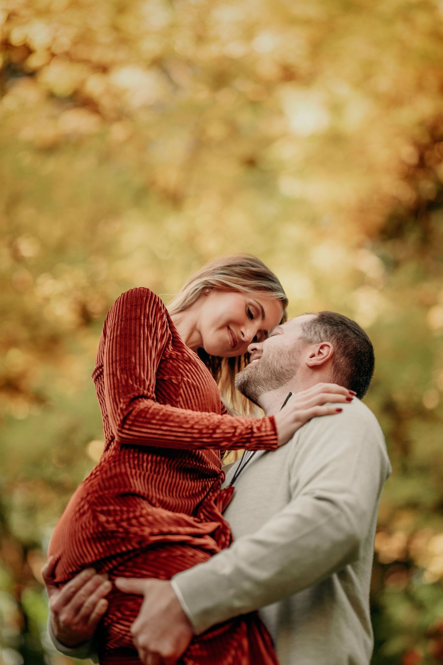 Couple embracing and smiling at each other surrounded by golden autumn foliage.