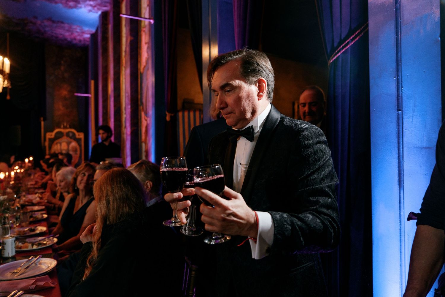 Tuxedo-clad waiter serving drinks at elegant candlelit wedding reception dinner.