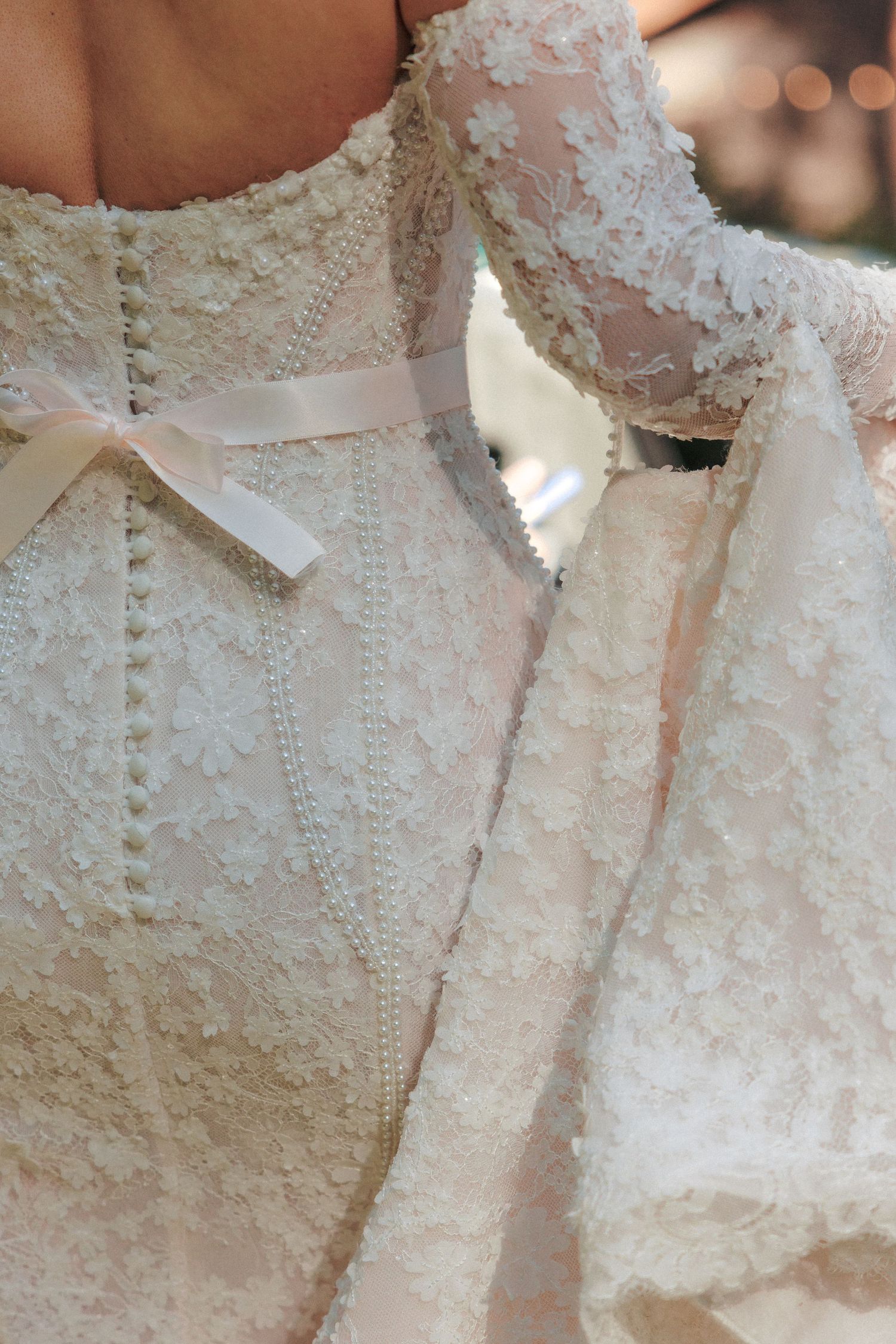Close-up detail of lace wedding gown back with pearl buttons and satin ribbon bow.
