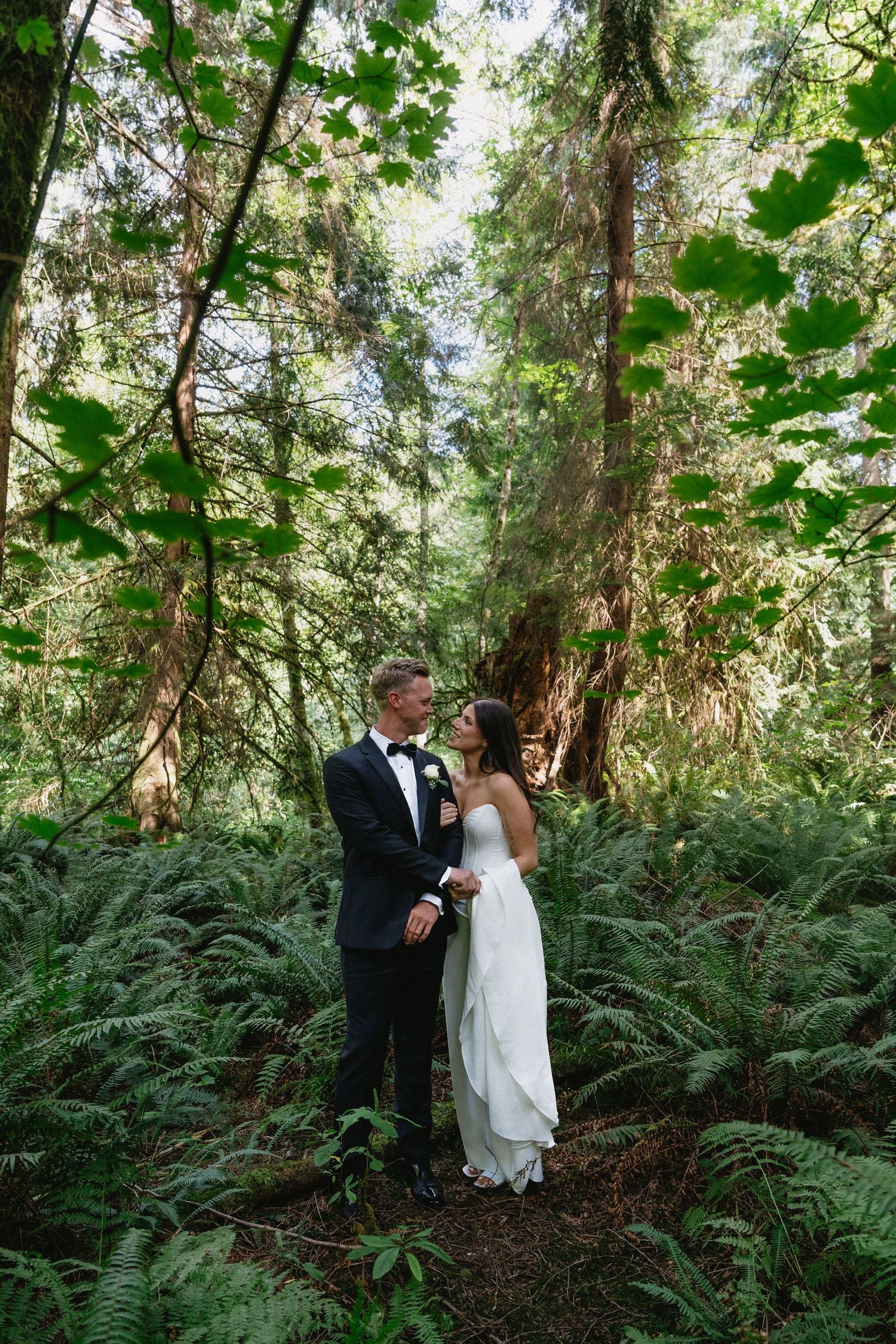 Bride and groom sharing romantic moment surrounded by lush ferns in enchanting forest setting.