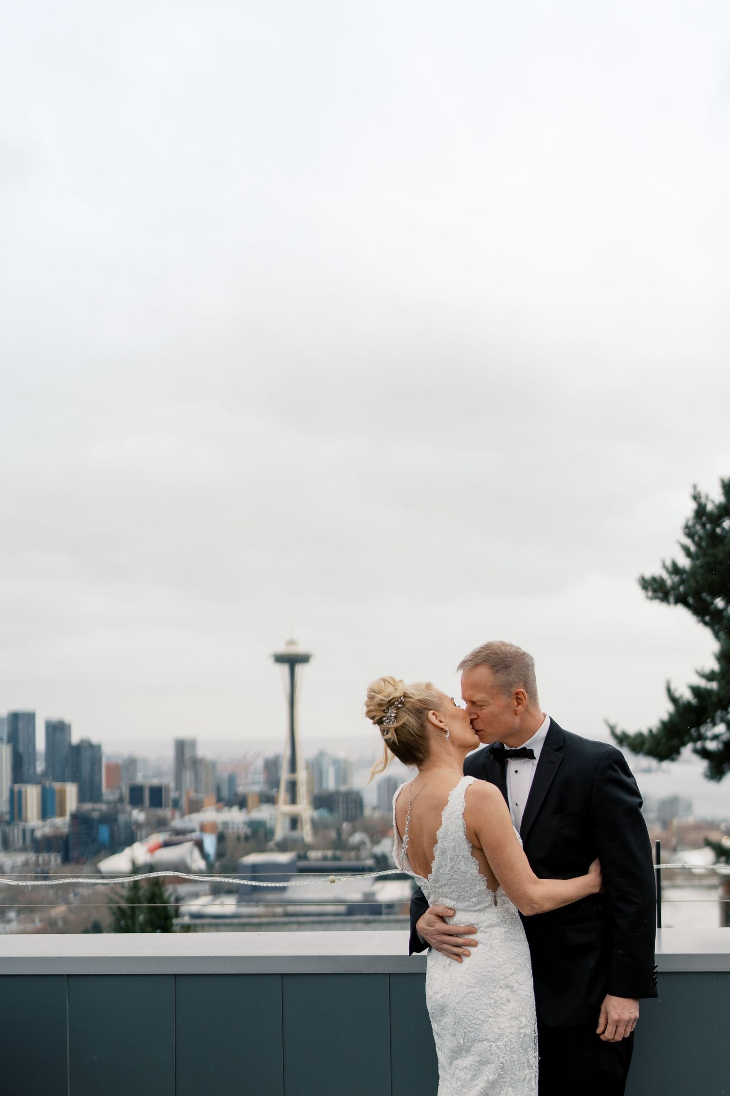 Bride and groom sharing a kiss on a rooftop with the Seattle Space Needle skyline in the background.
