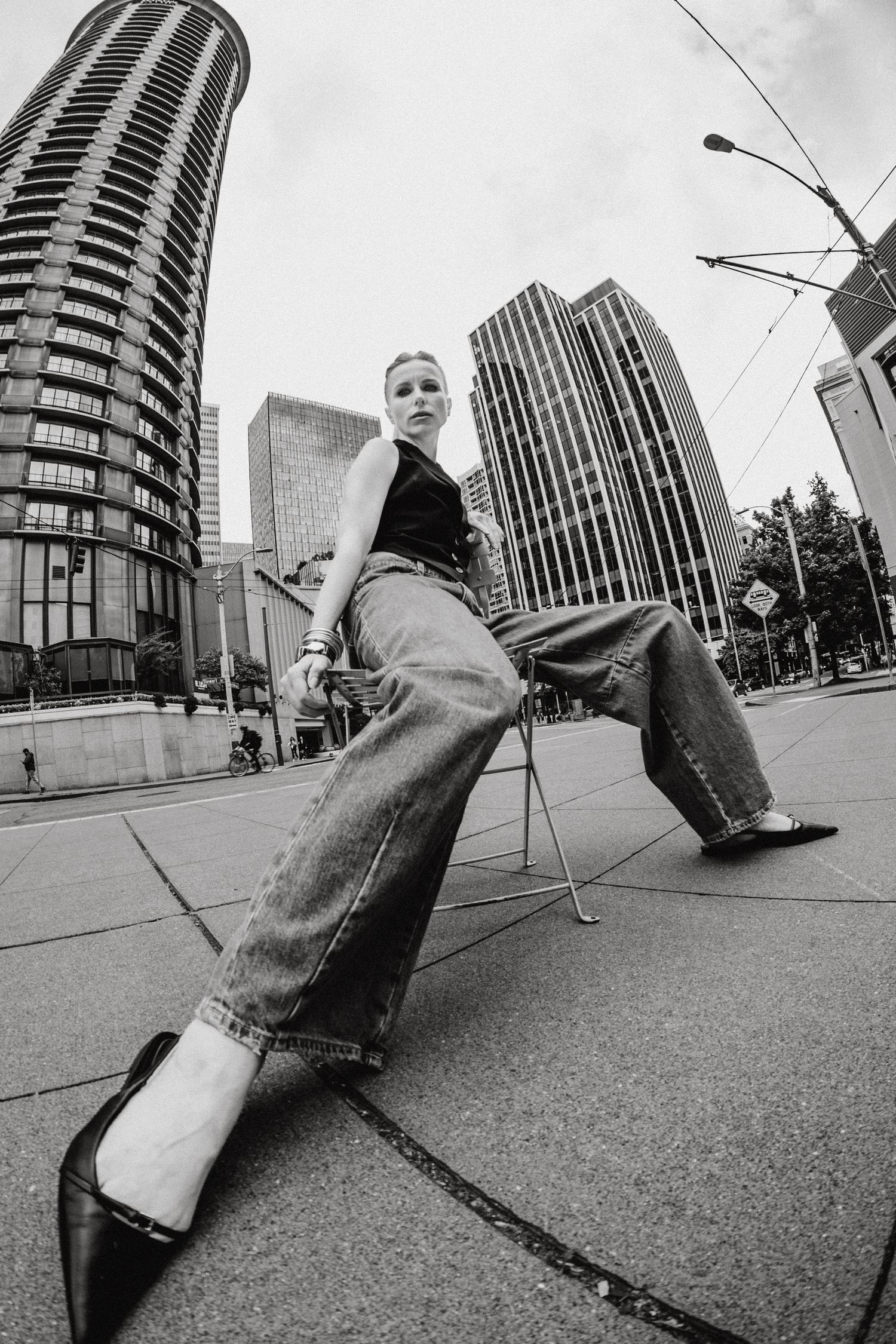 Woman in wide-leg jeans poses on city sidewalk with skyscrapers in black and white.