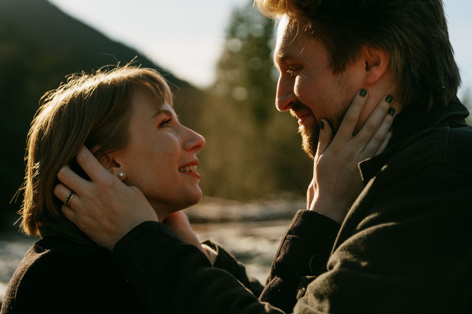 Couple facing each other tenderly, woman holding mans face, with mountain backdrop in golden light.