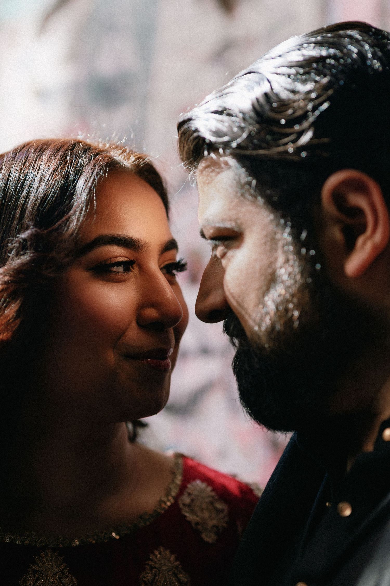 Close-up of South Asian couple nearly touching foreheads, surrounded by bokeh lights in a romantic moment.