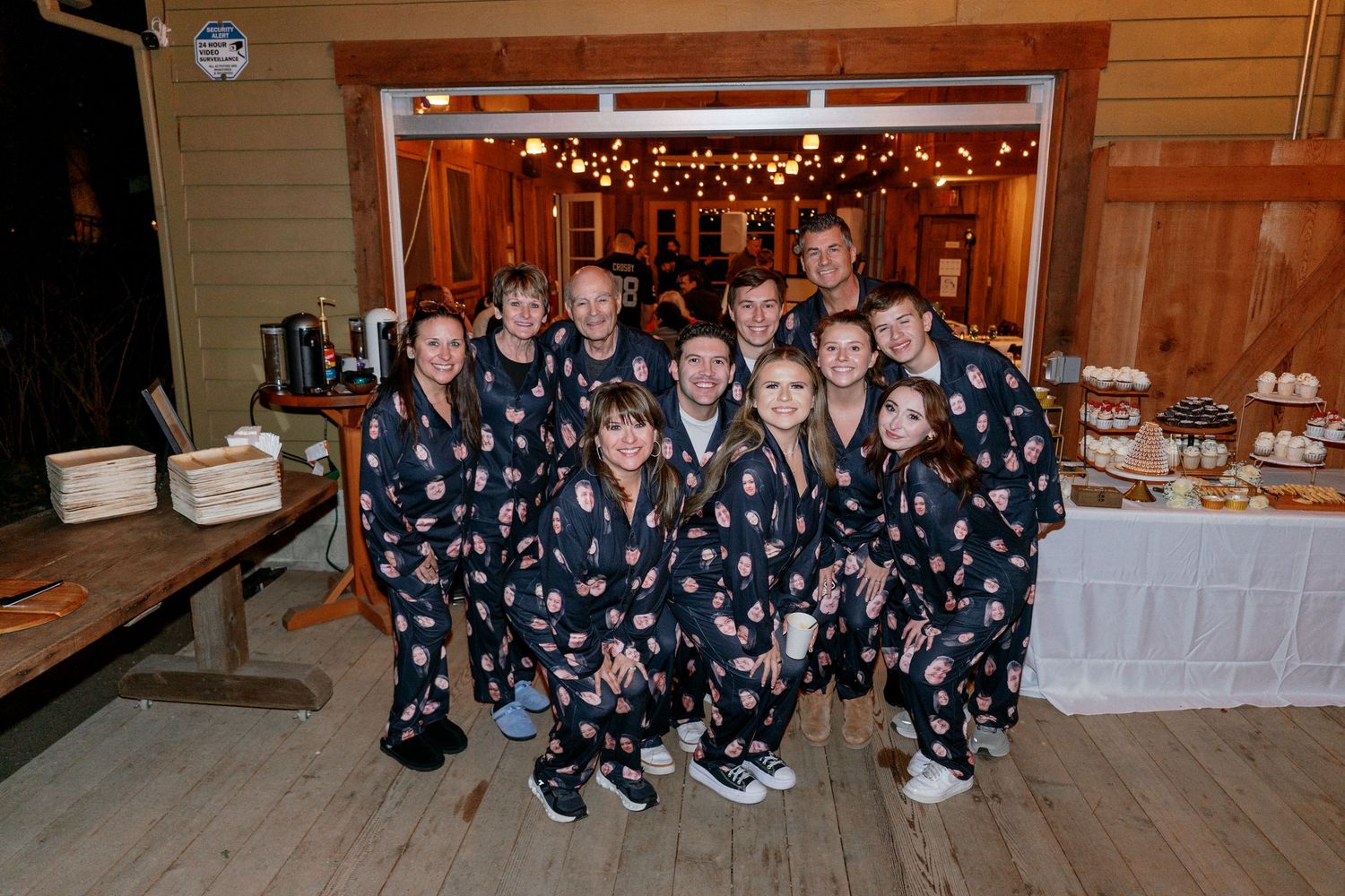 Wedding party group photo with guests wearing matching floral pajamas at a rustic barn wedding reception.