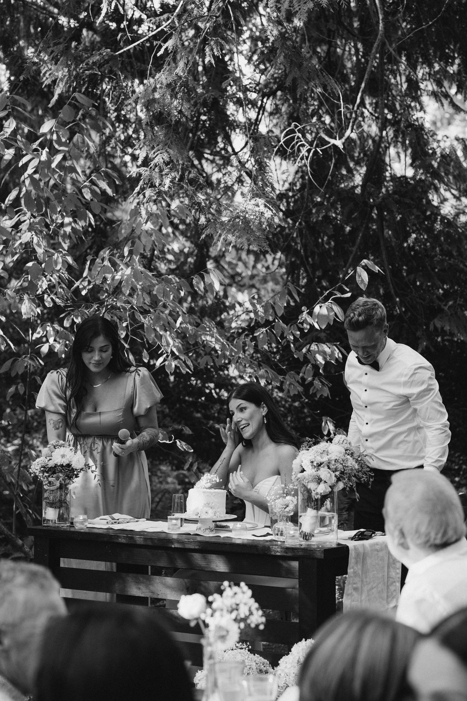 Black and white photo of bride and groom at sweetheart table during outdoor wedding reception.
