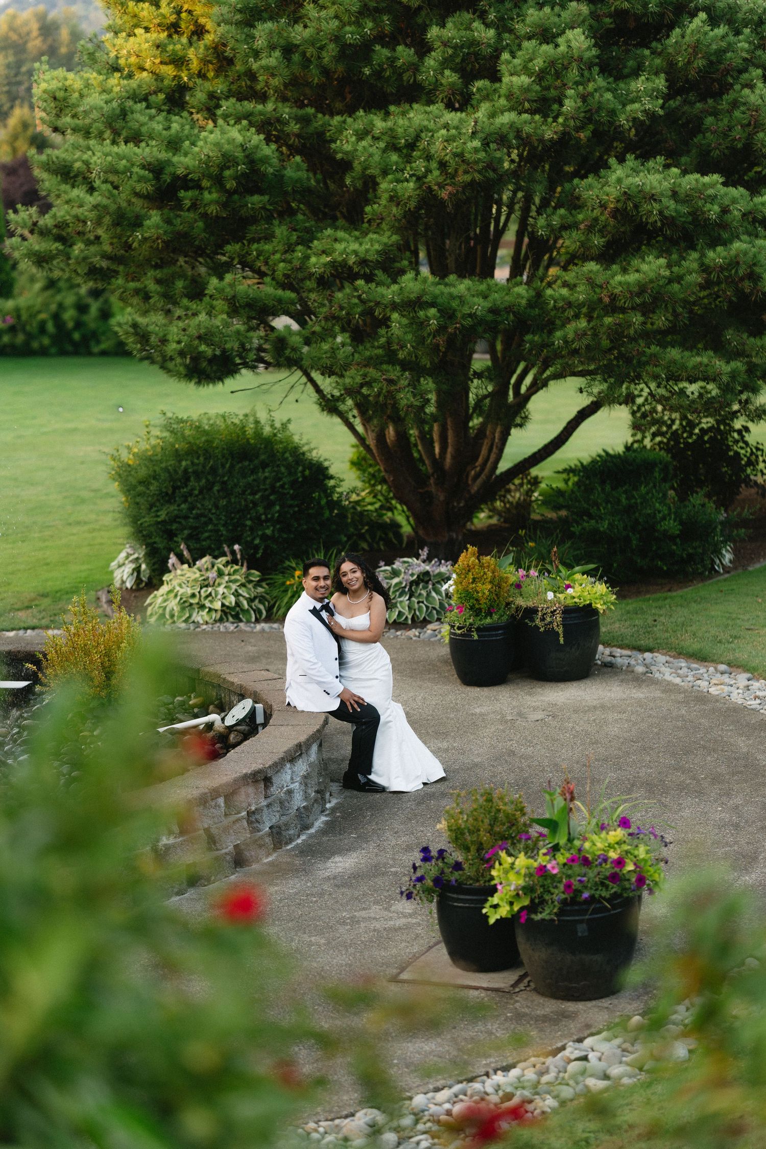 Bride and groom pose together in a lush garden setting surrounded by colorful flowers and greenery.