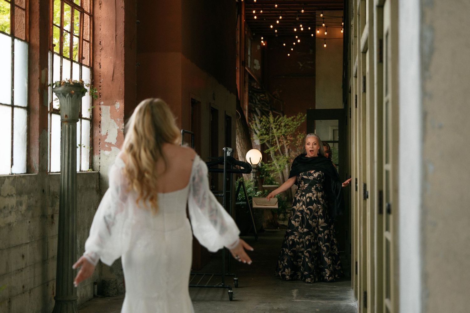 Bride in white lace gown sharing an emotional first look moment in a rustic venue with string lights.
