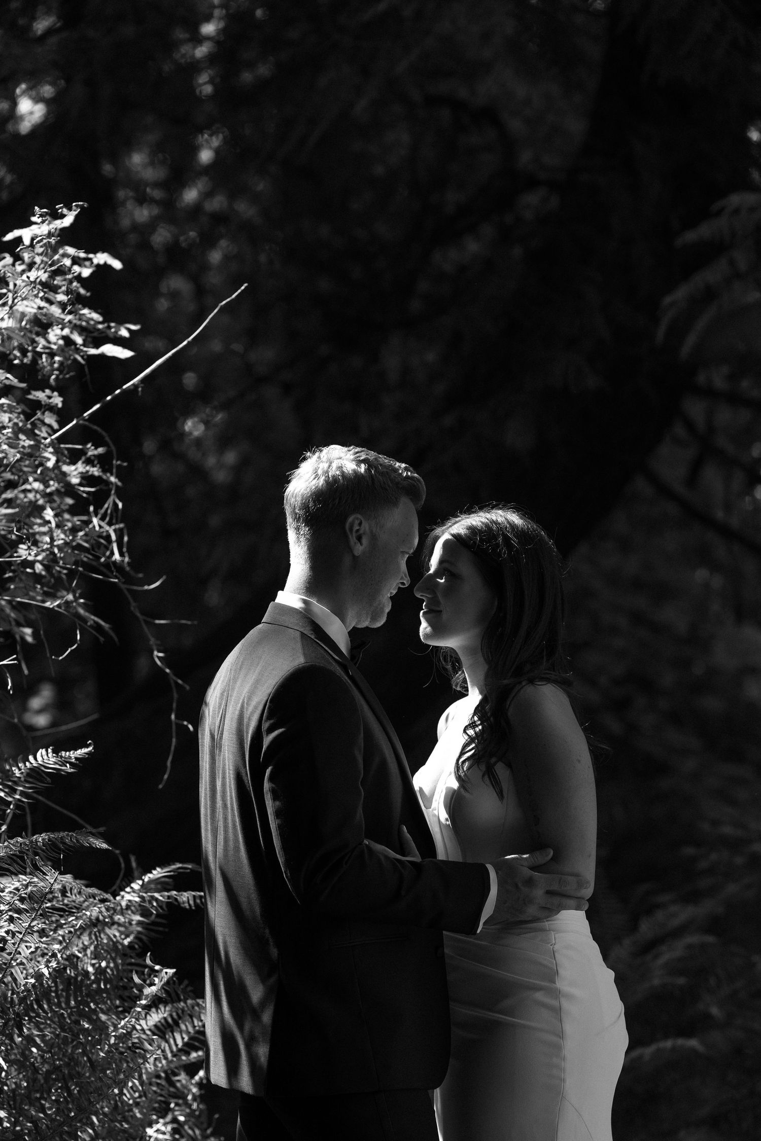 Black and white portrait of bride and groom facing each other in forest.