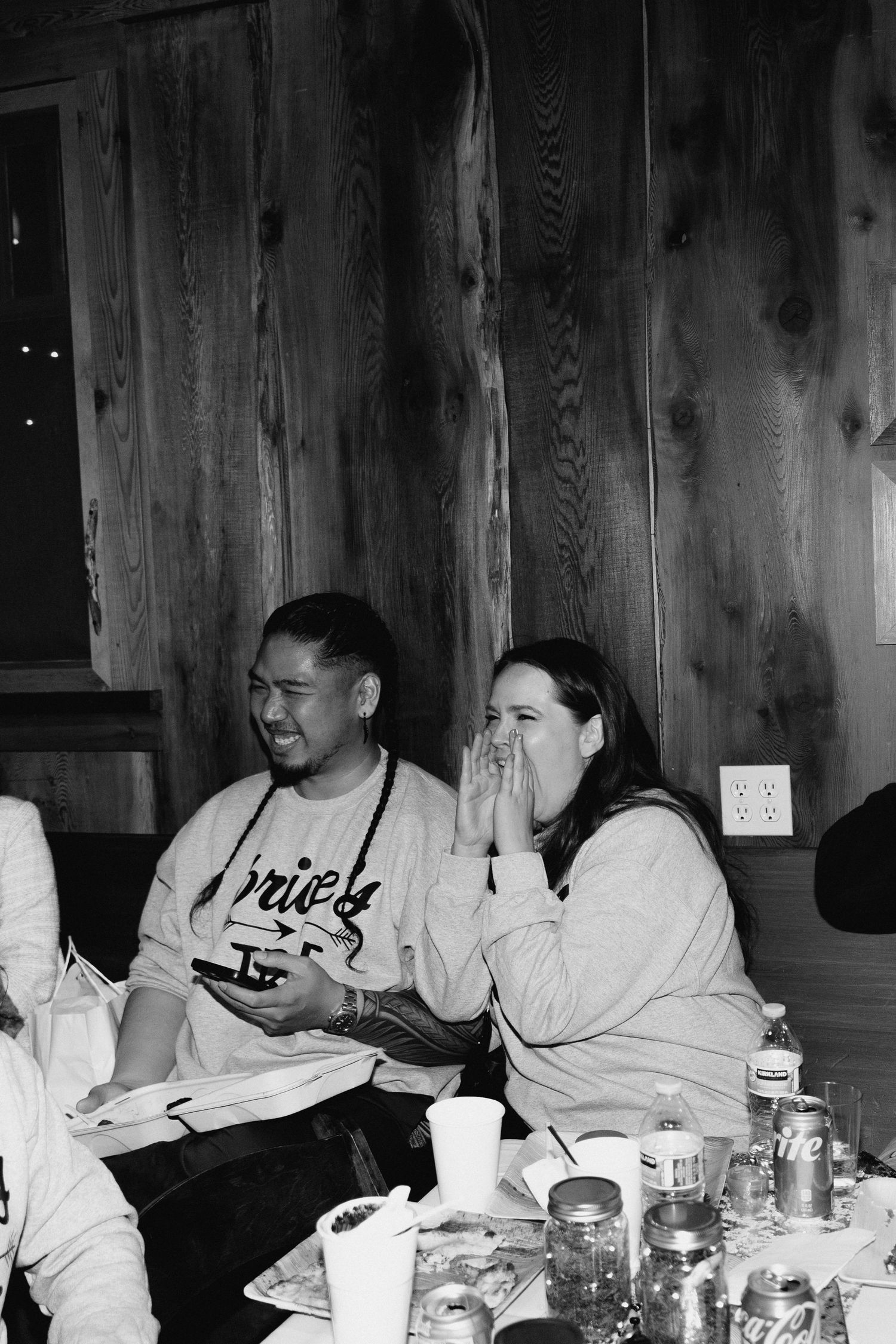 Couple laughing together at a casual wedding rehearsal dinner seated at a table with drinks.