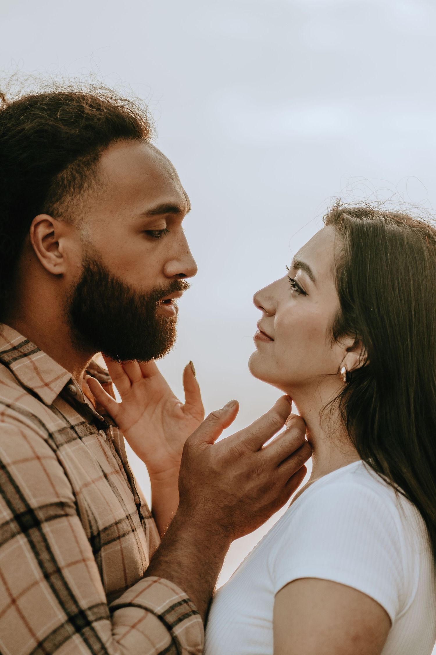 Intimate close-up of a bearded man tenderly holding a woman's face as they gaze into each other's eyes.