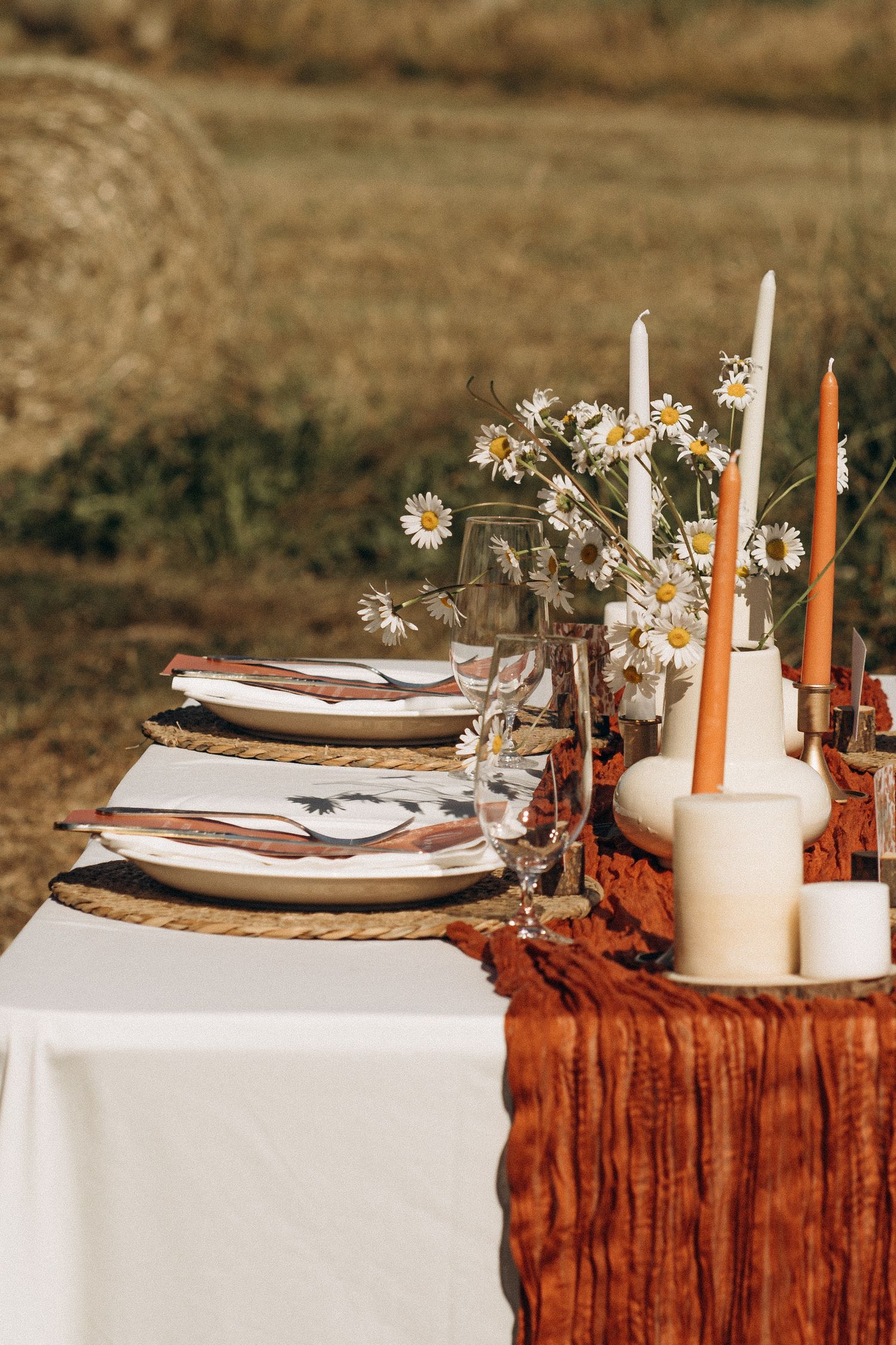 Rustic outdoor wedding table with daisies, orange candles, and wicker charger plates.