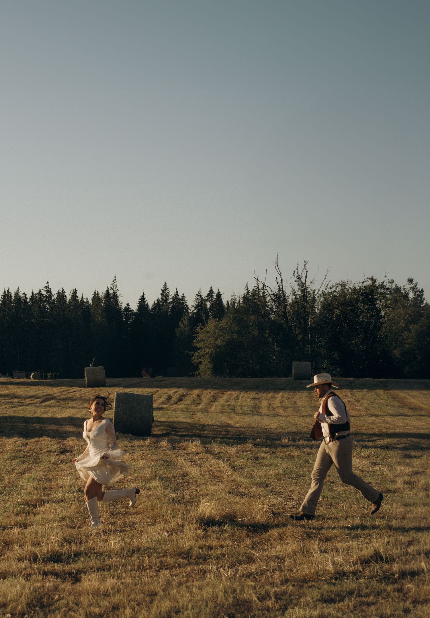 Bride and groom playfully running toward each other in open golden field at dusk.
