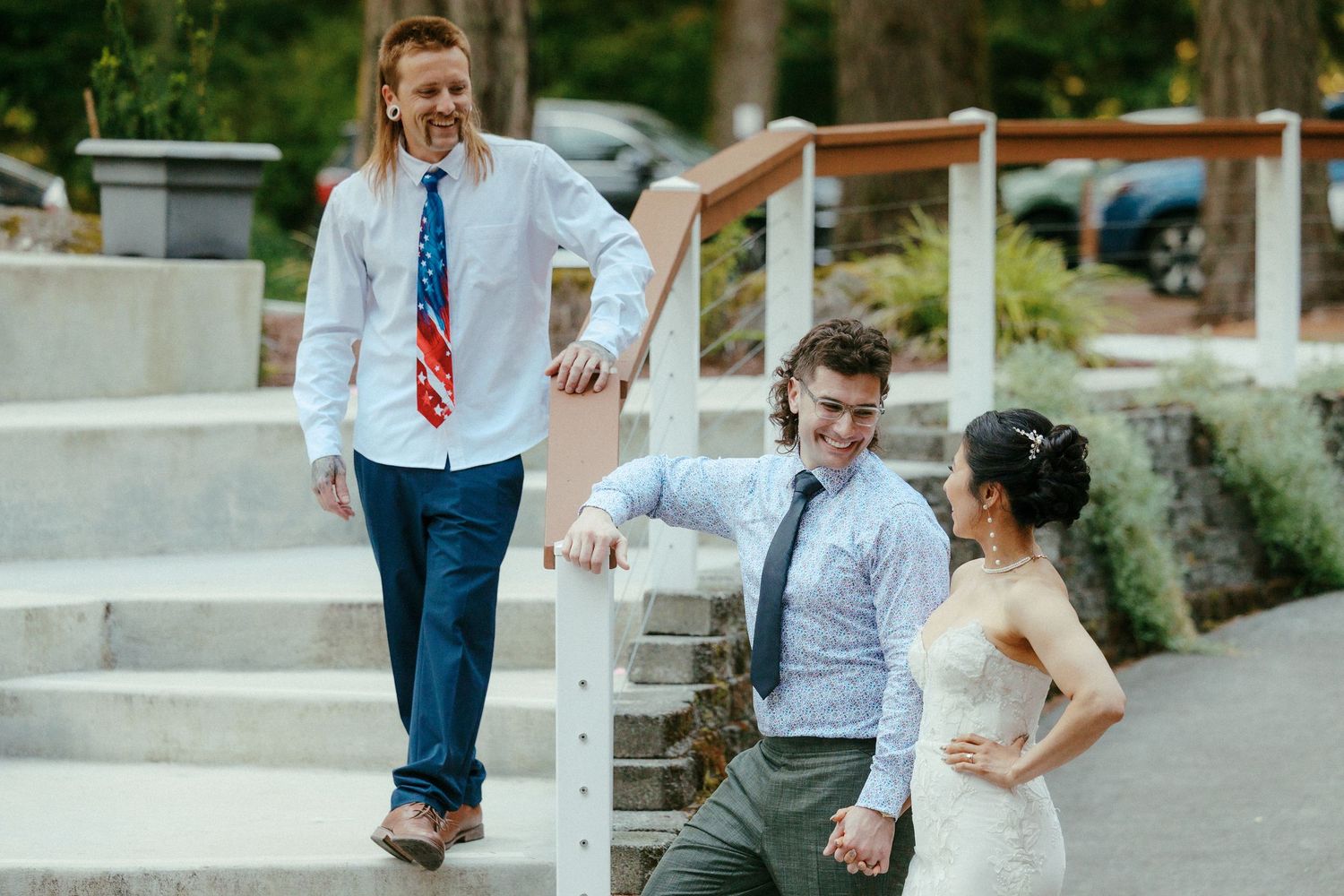 Bride in white gown laughs with two young men in ties on outdoor wedding venue steps.