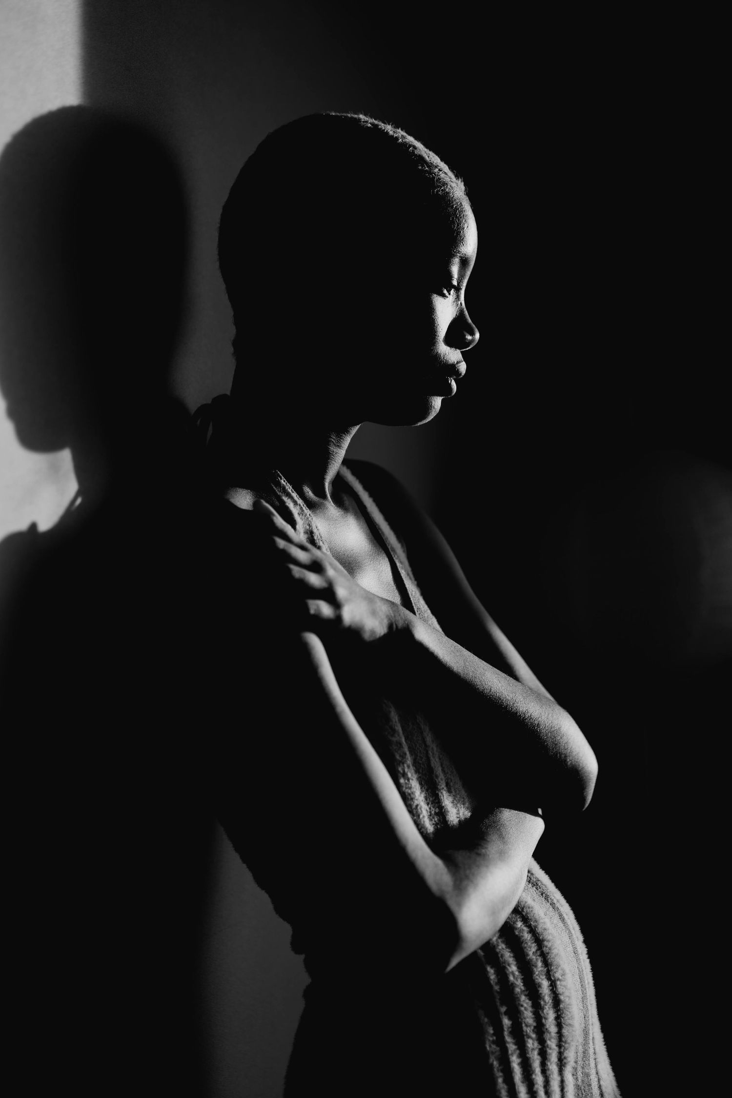 Moody black and white profile portrait of a woman with short hair crossing her arms in dramatic lighting.