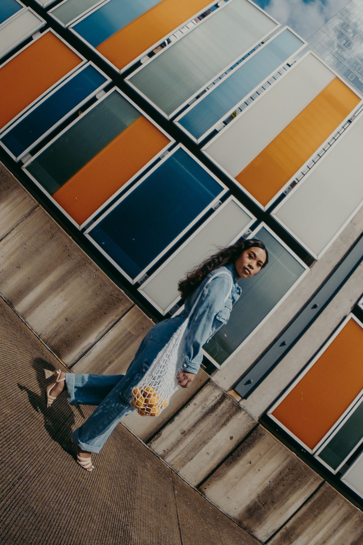Woman in denim jeans and jacket stands before a vibrant geometric colorful panel wall, shot from above.