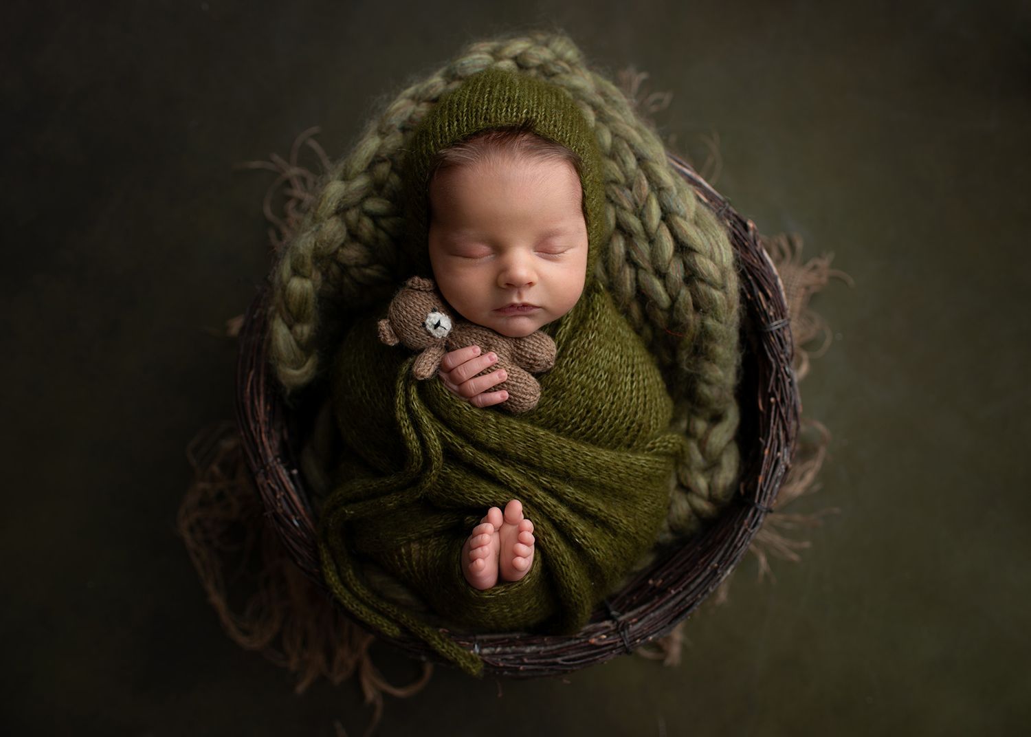 Sleeping newborn wrapped in green blanket woven basket with teddy bear, soft studio lighting, Victoria BC newborn photography