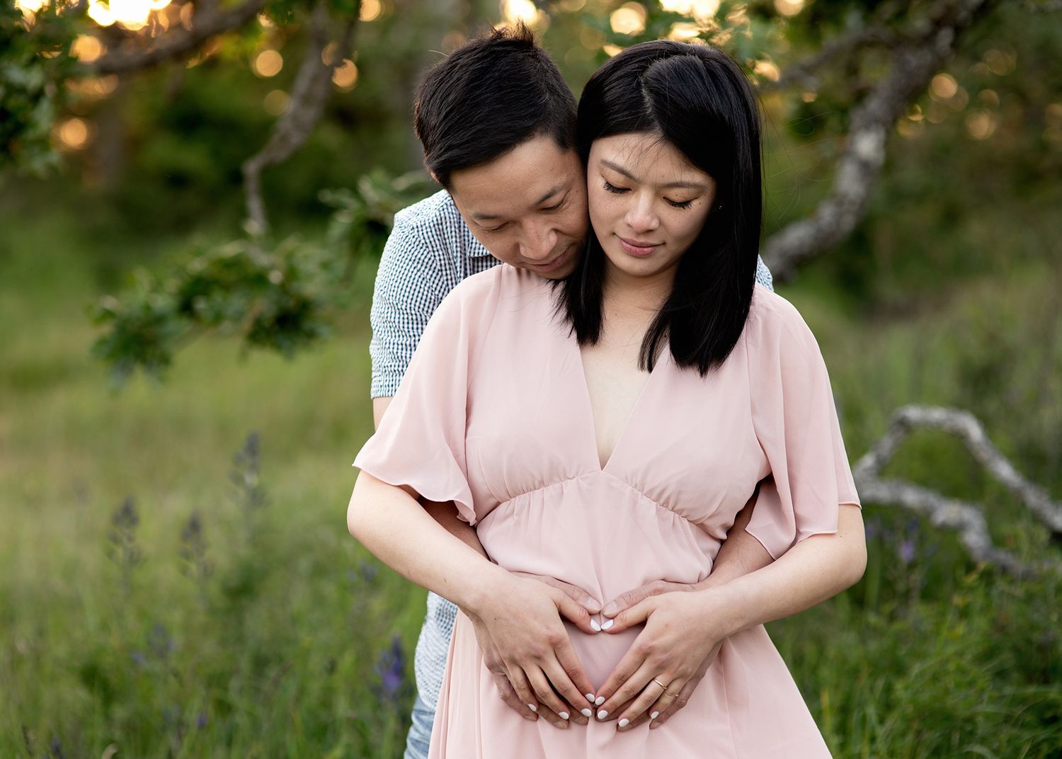 Couple in pink maternity dress embraces during sunset outdoor photo session in a lush garden setting, Victoria BC maternity photography