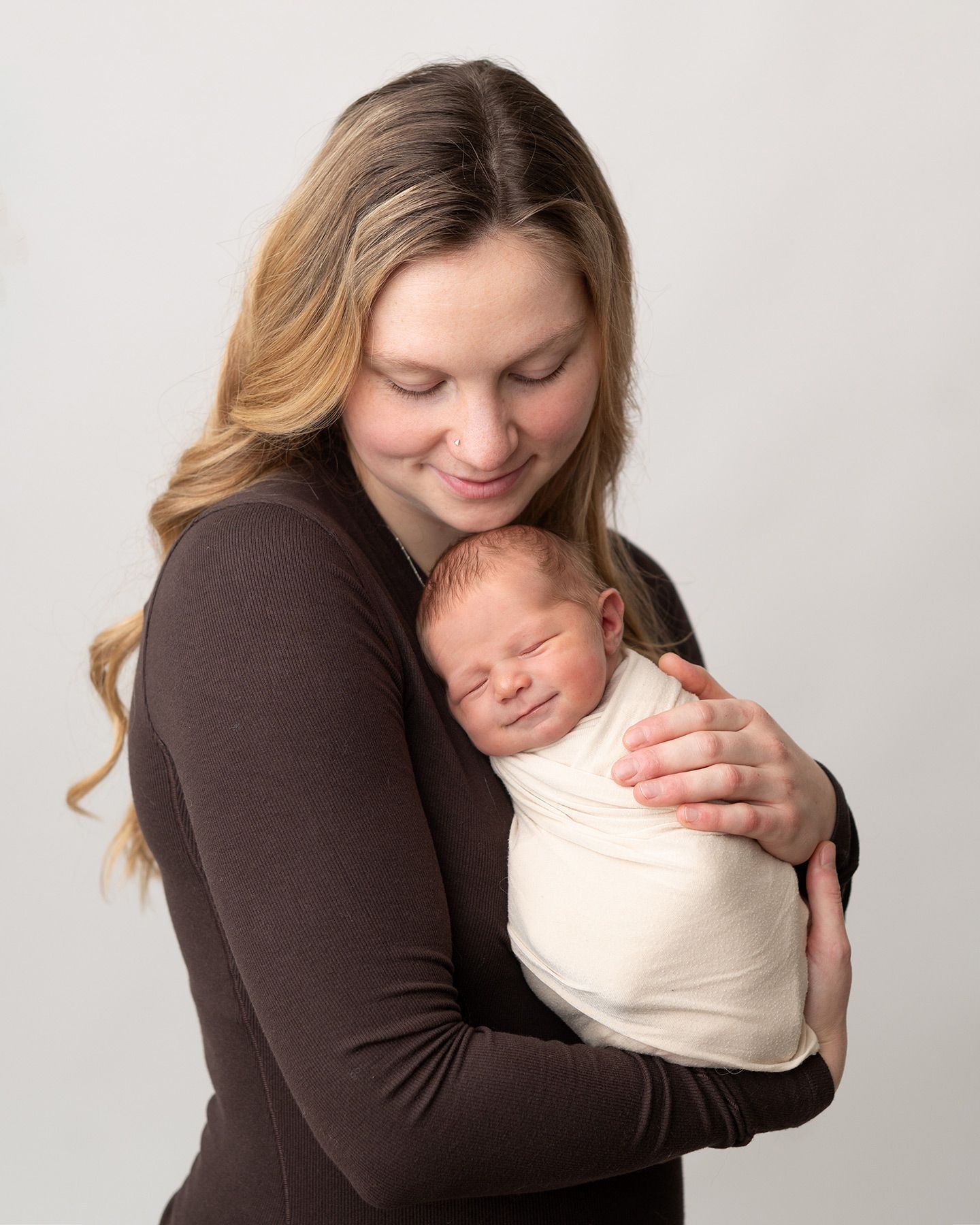 mother holding a smiling newborn baby wrapped in soft fabric, warm studio session, Victoria BC