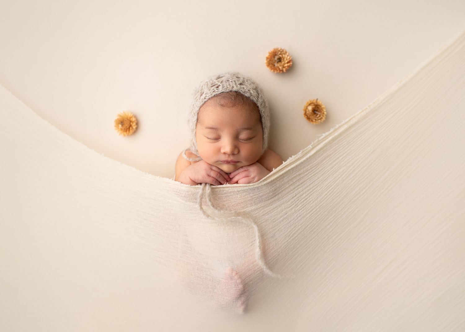 A sleeping newborn tucked under a  cream-colored  blanket with small peach flowers scattered around, Victoria BC newborn photographer